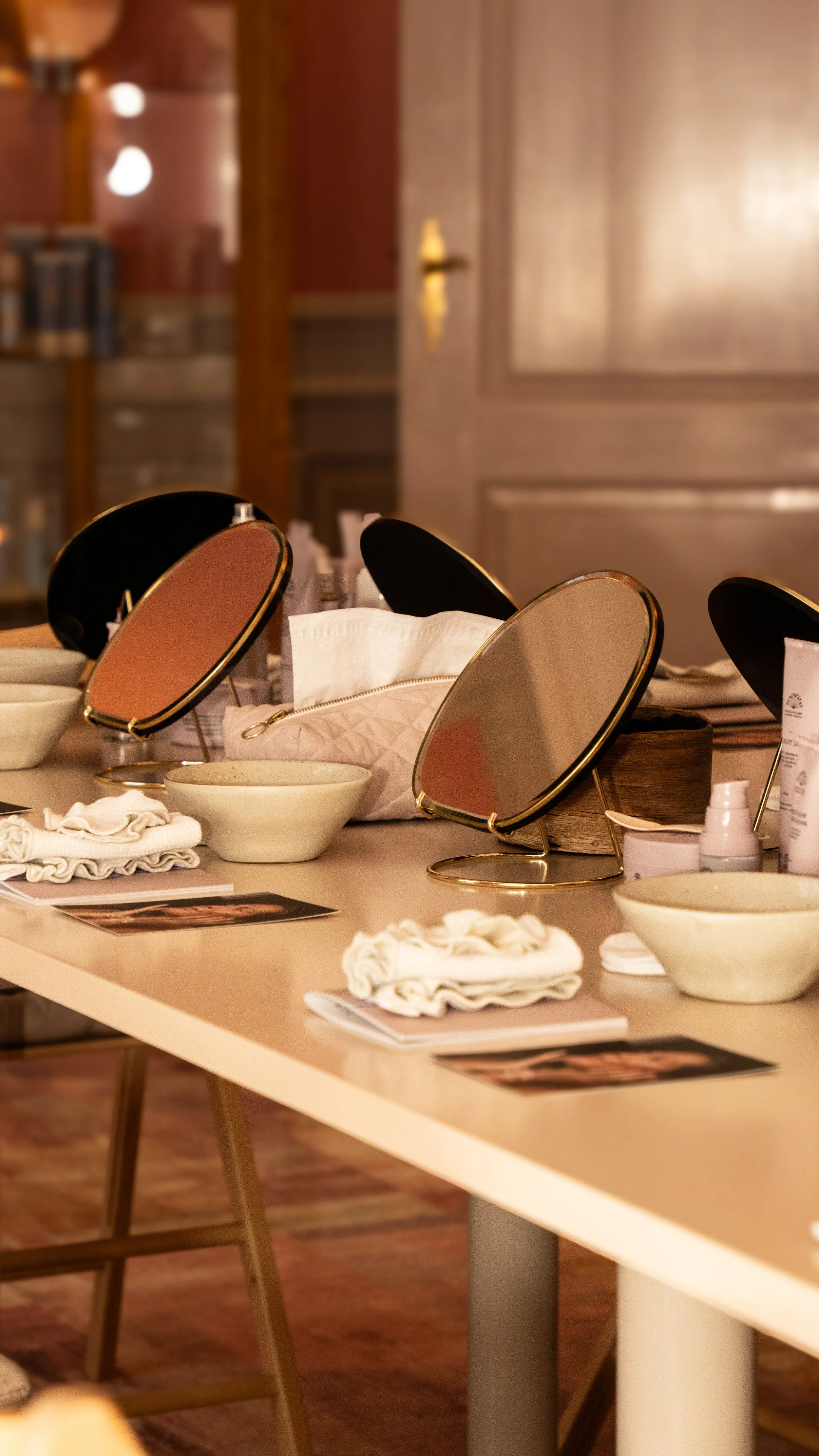 Et bord med spejle, skåle, håndklæder, ansigtsprodukter og brochurer, sandsynligvis for en skønhedssalon eller spa.