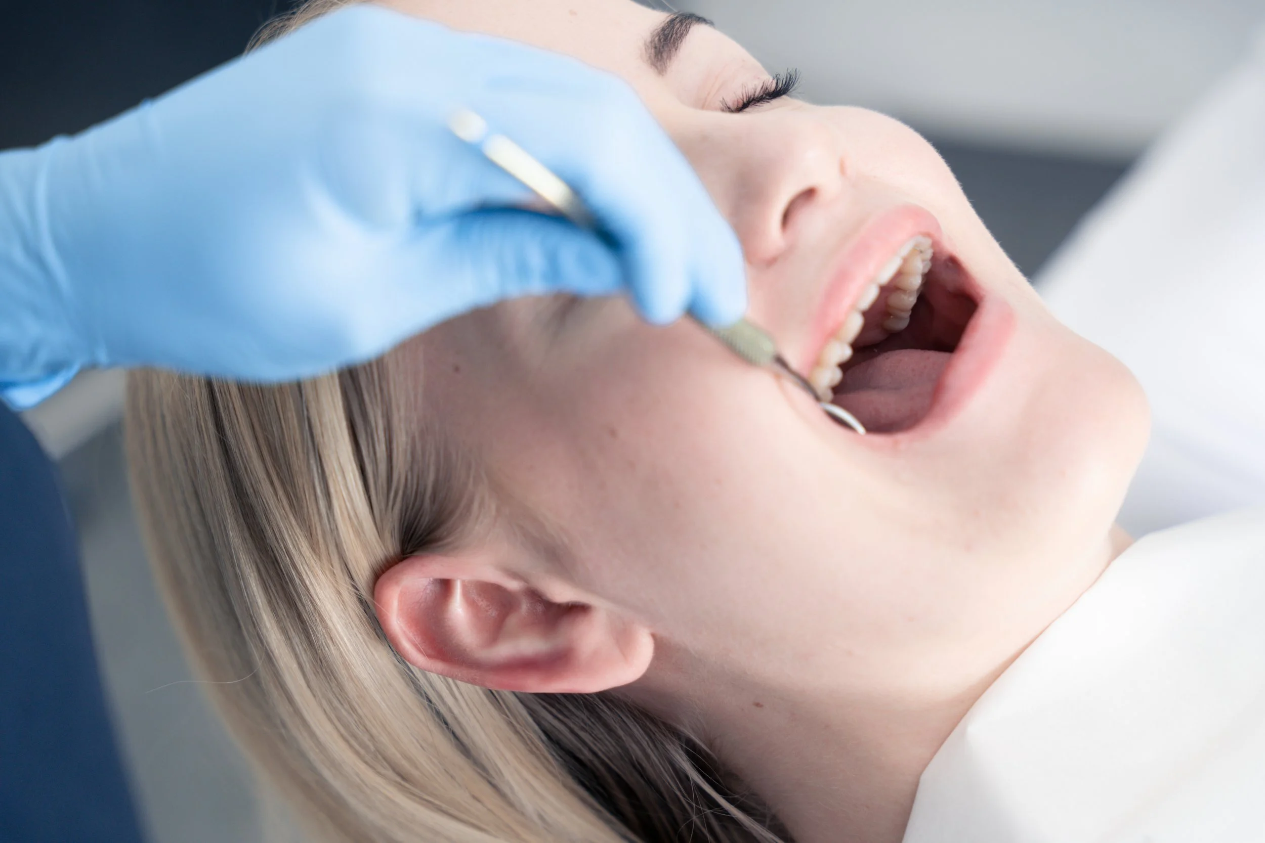 En kvinde ligger med åben mund hos en tandlæge, som bruger en dentalinstrument.