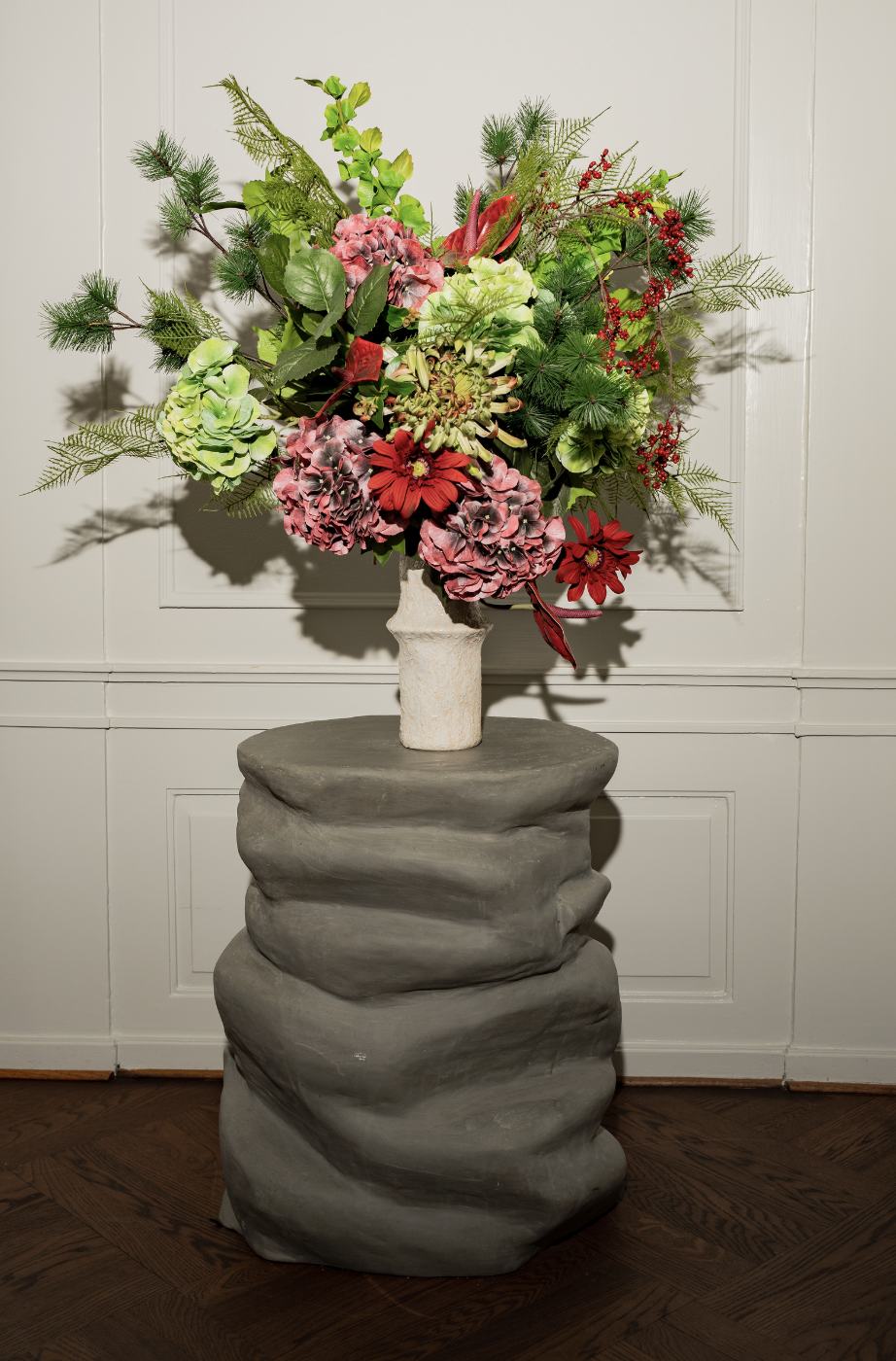 En stor buket med blomster og granblade i en vaser stående på en sten base.