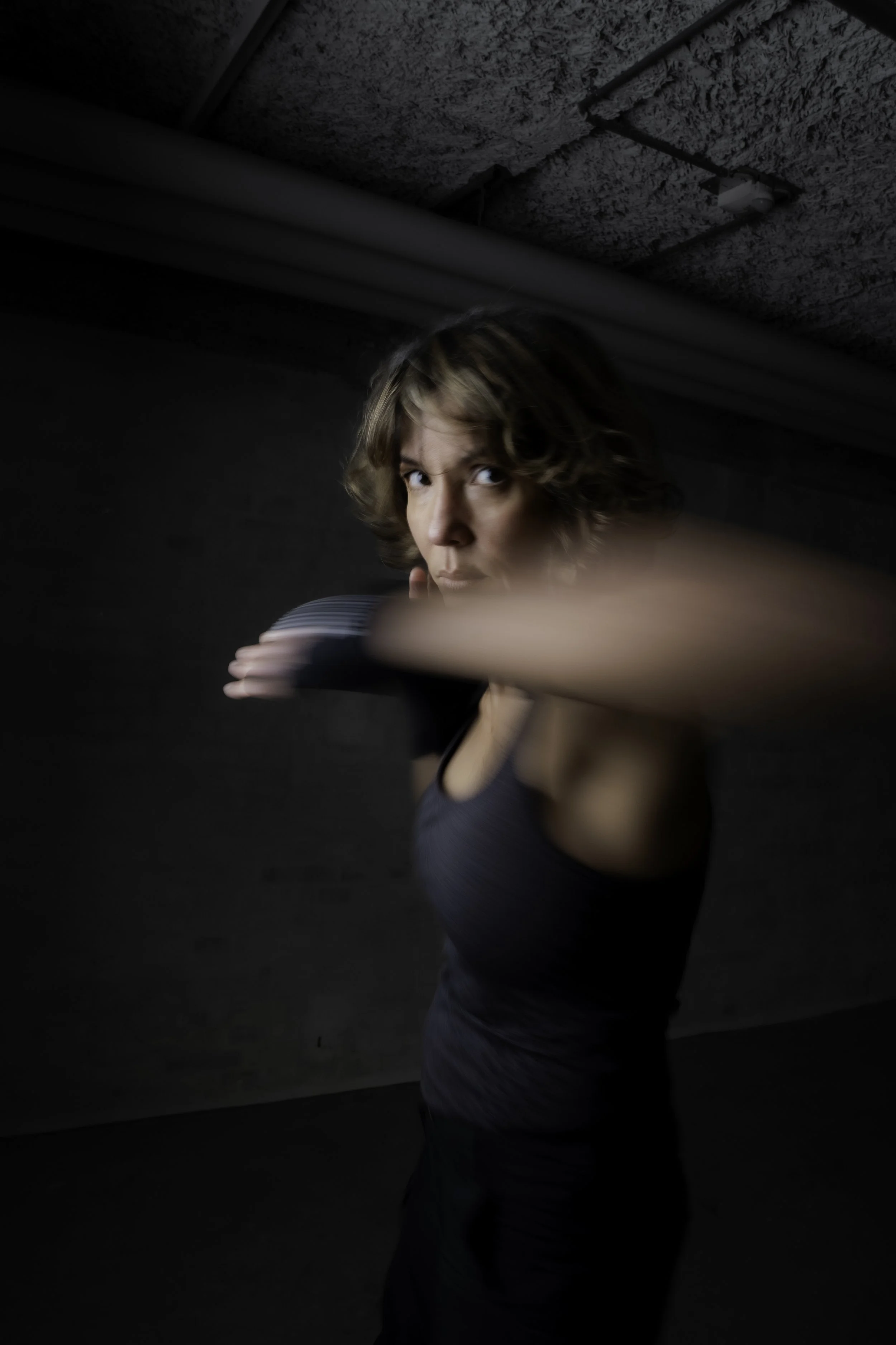 En kvinde i træning med fokus, i sort træningstøj, udfører en bokseøvelse i et mørkt rum.