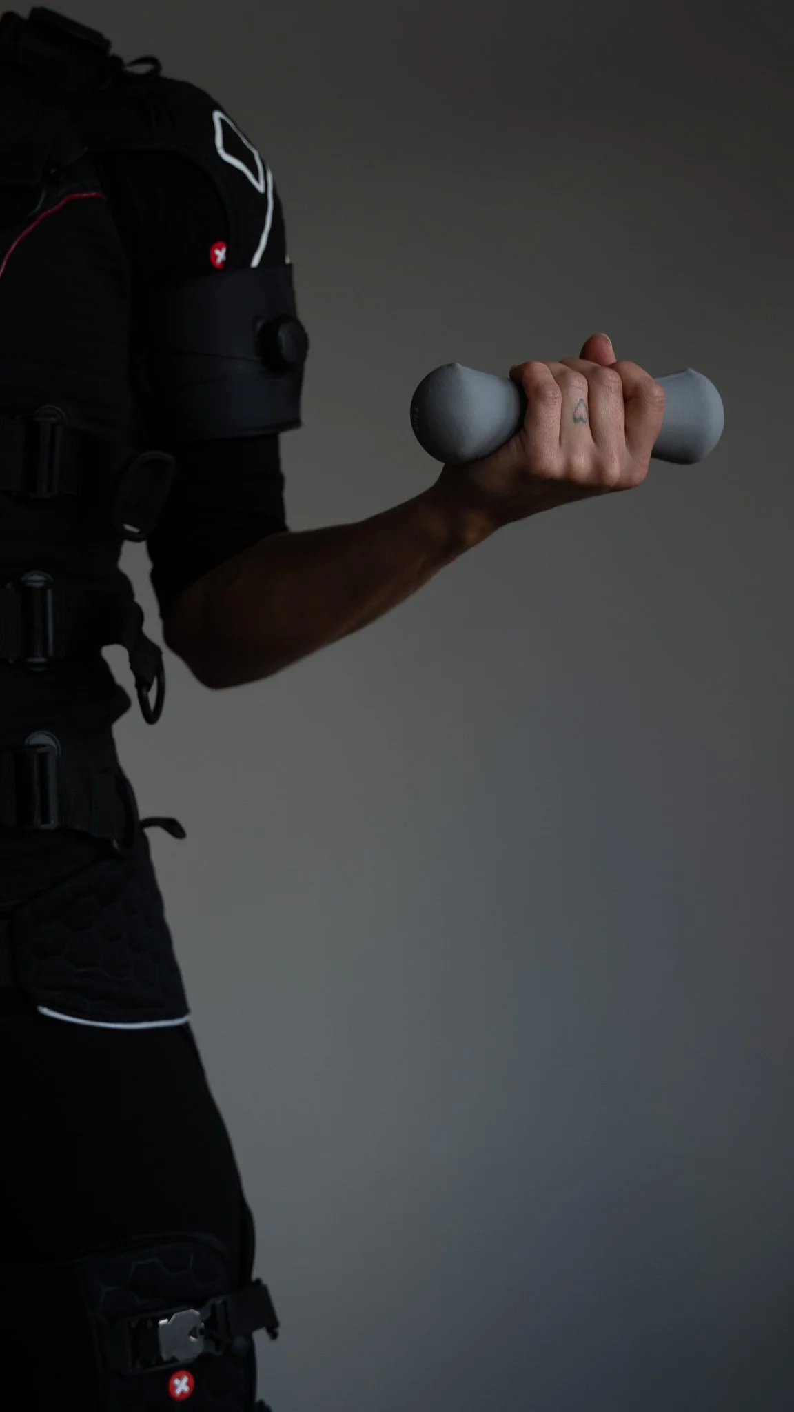 En person holder en grå vægt i hånden, iført sort sportsudstyr.