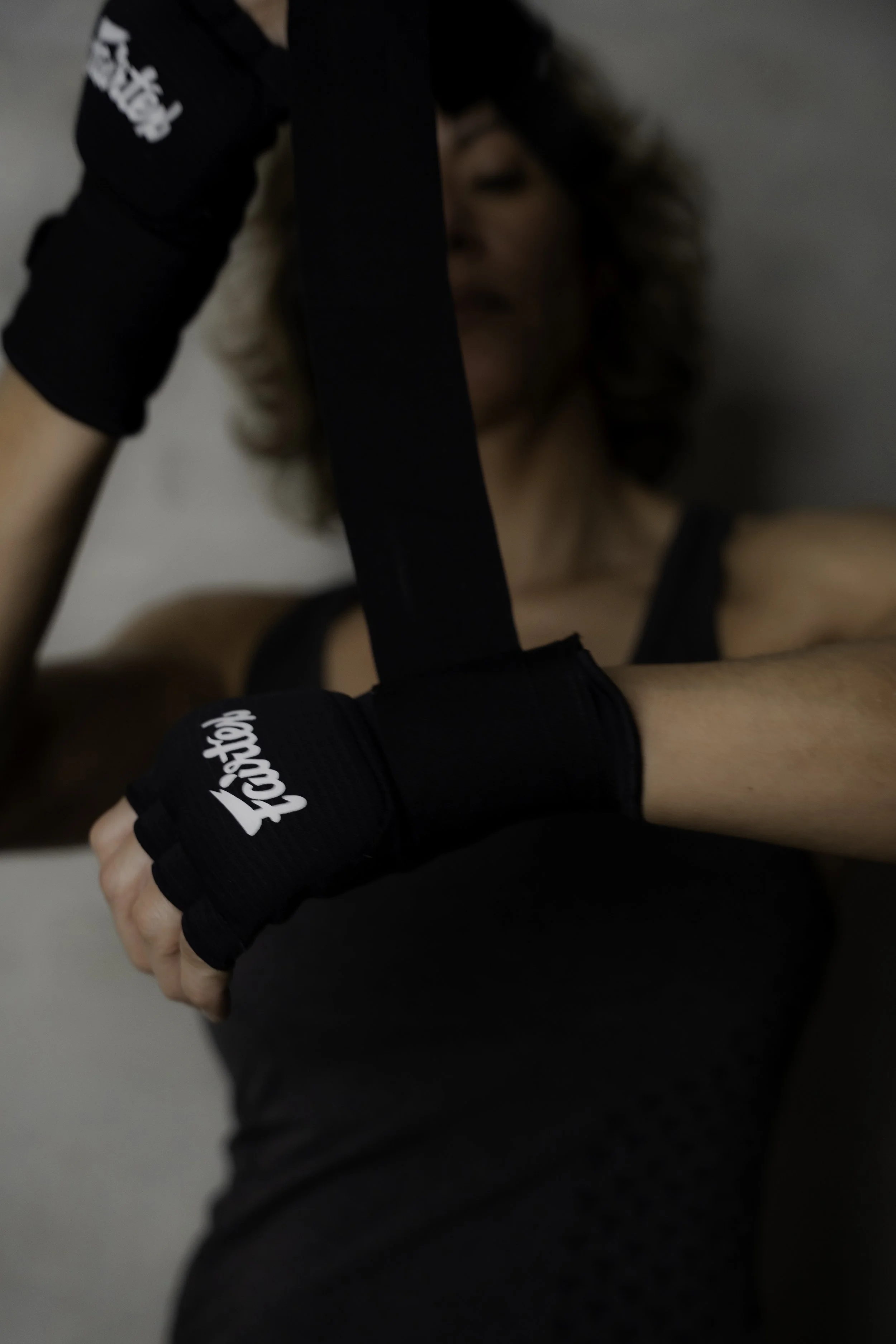 Kvinde i træningstøj med sorte handsker, der trækker en træningsrem, tæt opkaldt, baggrundsdybt, fokus på træningsremmen.