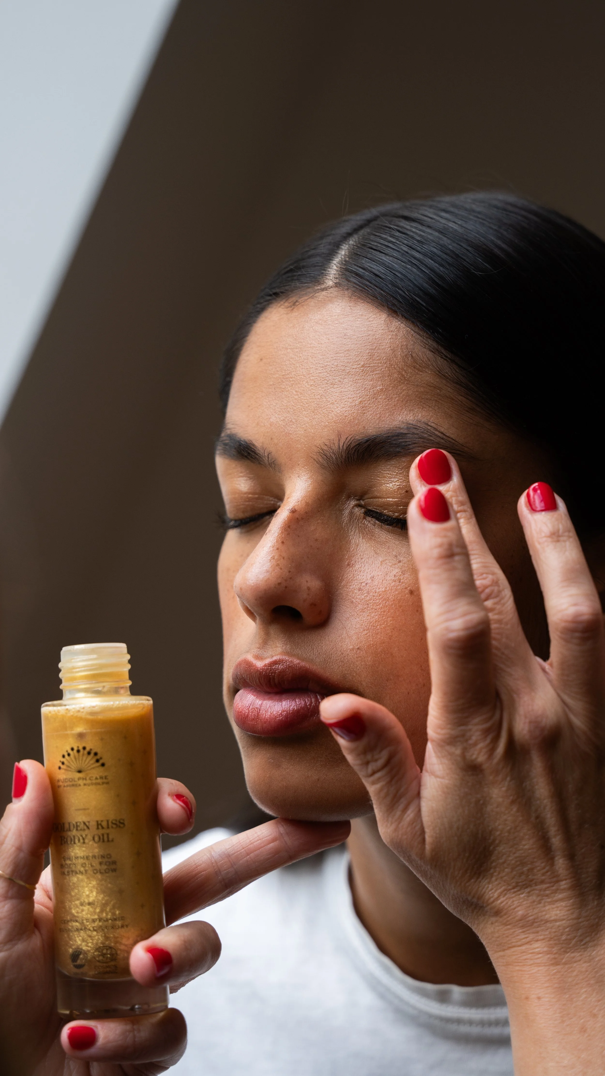 En kvinde med lukket øjne, der bruger et produkt på ansigtet, mens hun holder en flaske med produktet.