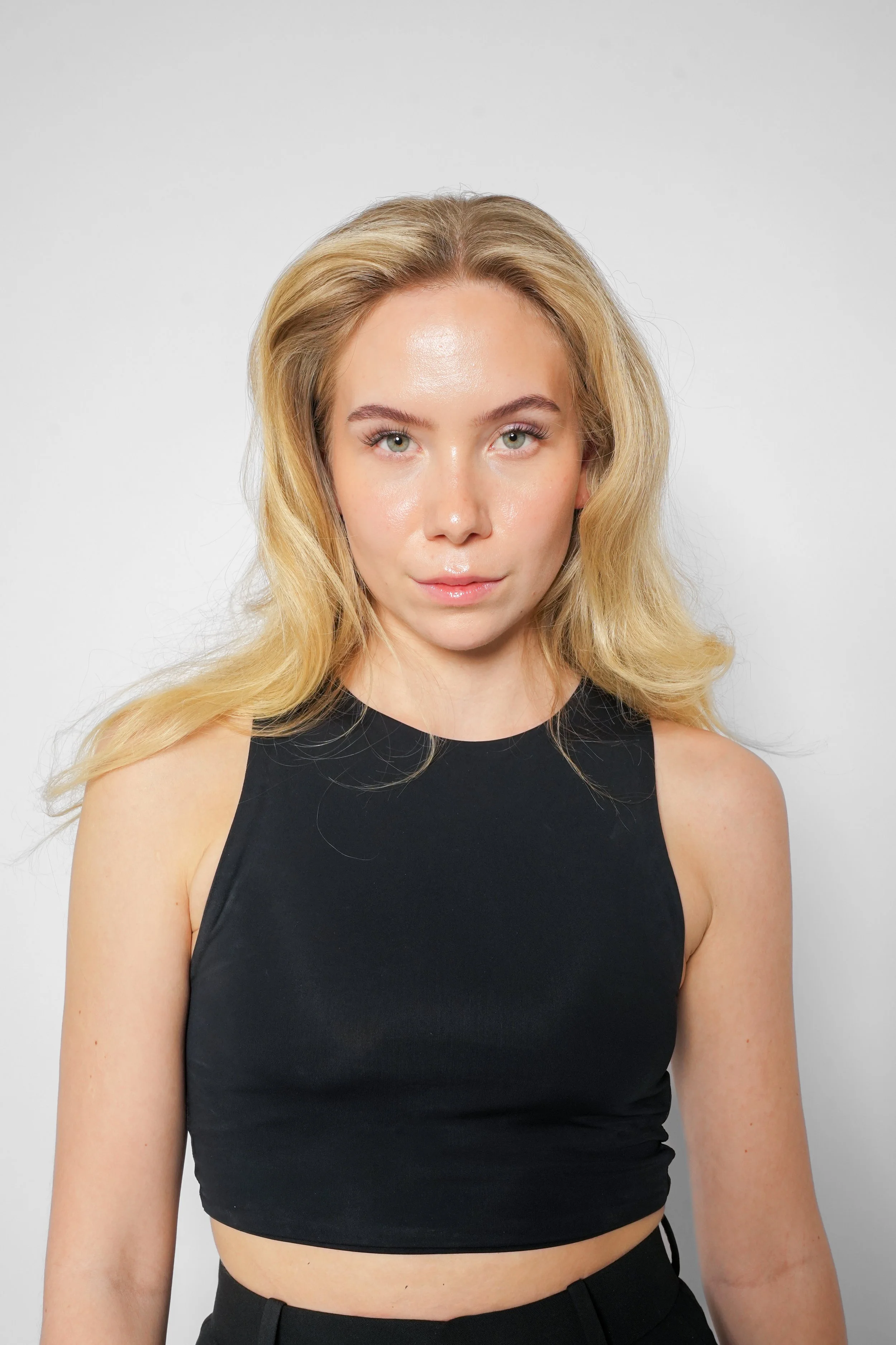 En ung kvinde med blond, bølget hår og grønne øjne, iført en sort top, står foran en hvid baggrund.