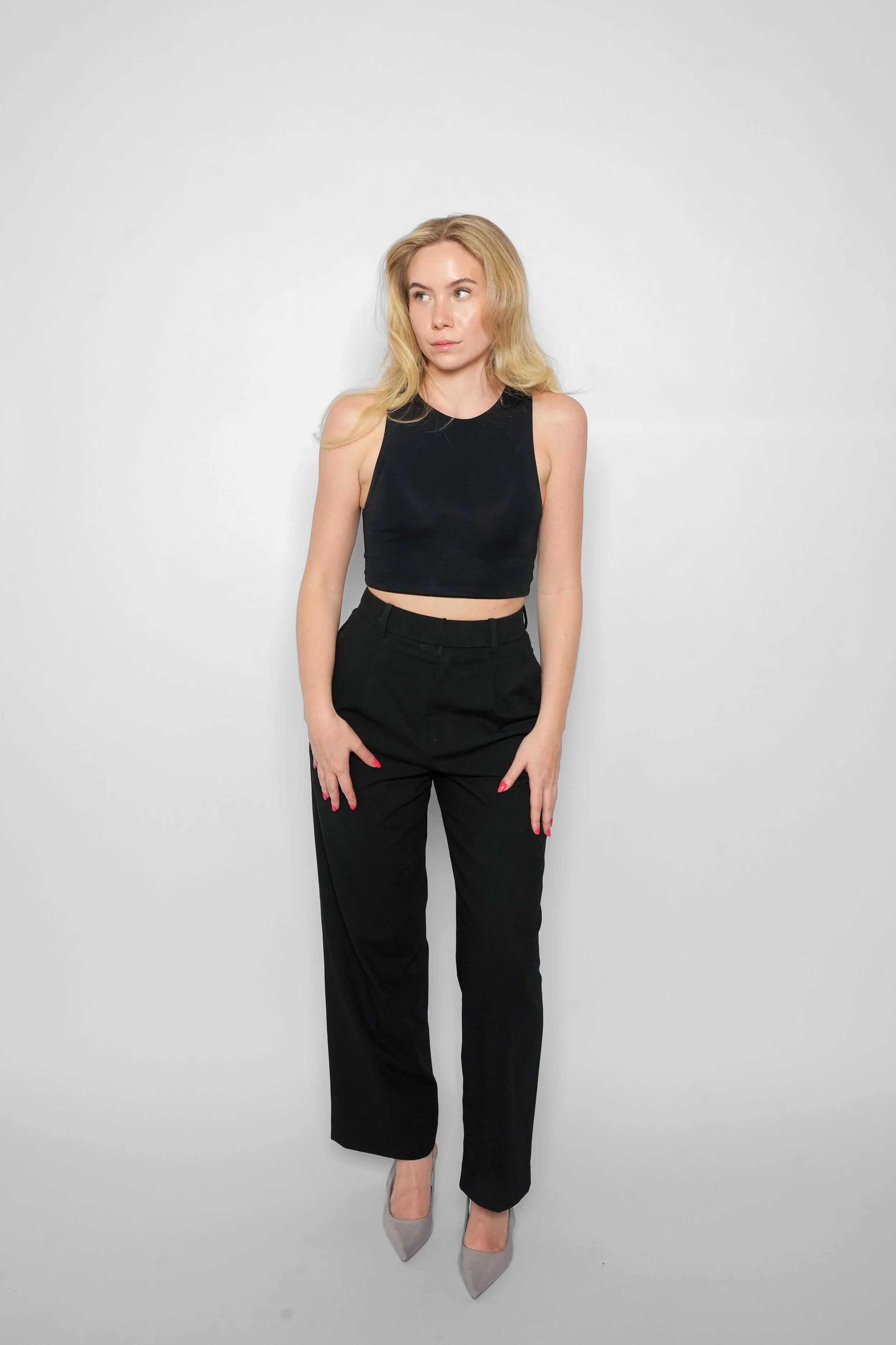 En ung kvinde med blond hår, iført sort top og sorte bukser stående mod en hvid baggrund.