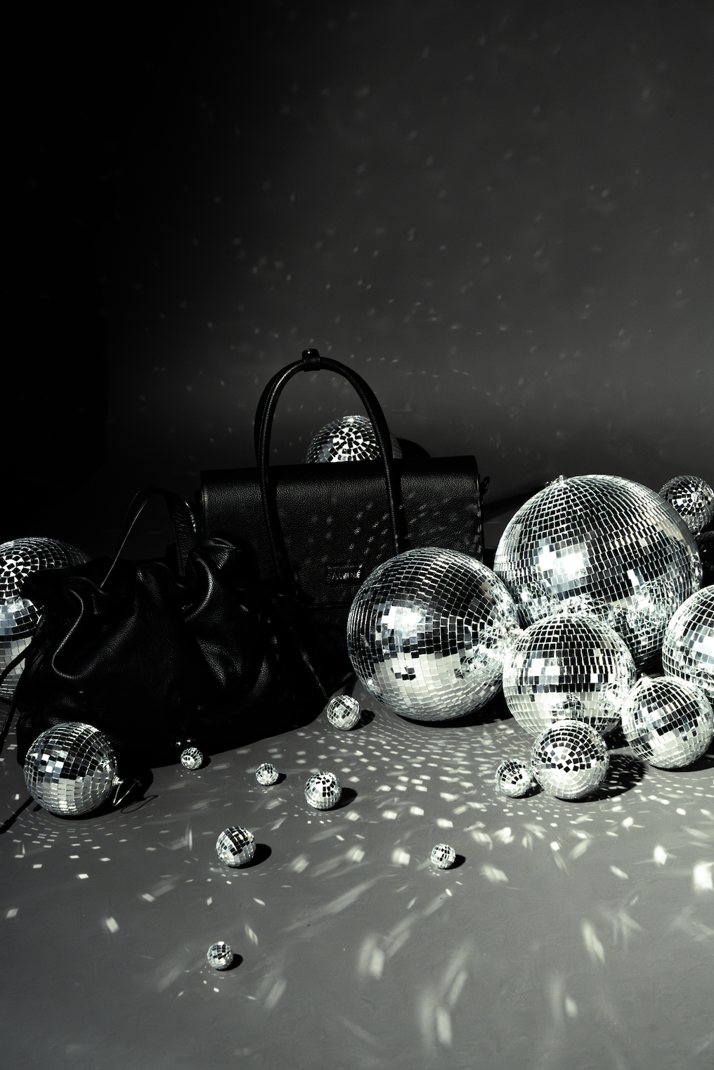 En sort håndtaske omgivet af flere små og store diskokugler , der spejler lyset og skaber reflekterede mønstre på den mørke baggrund.