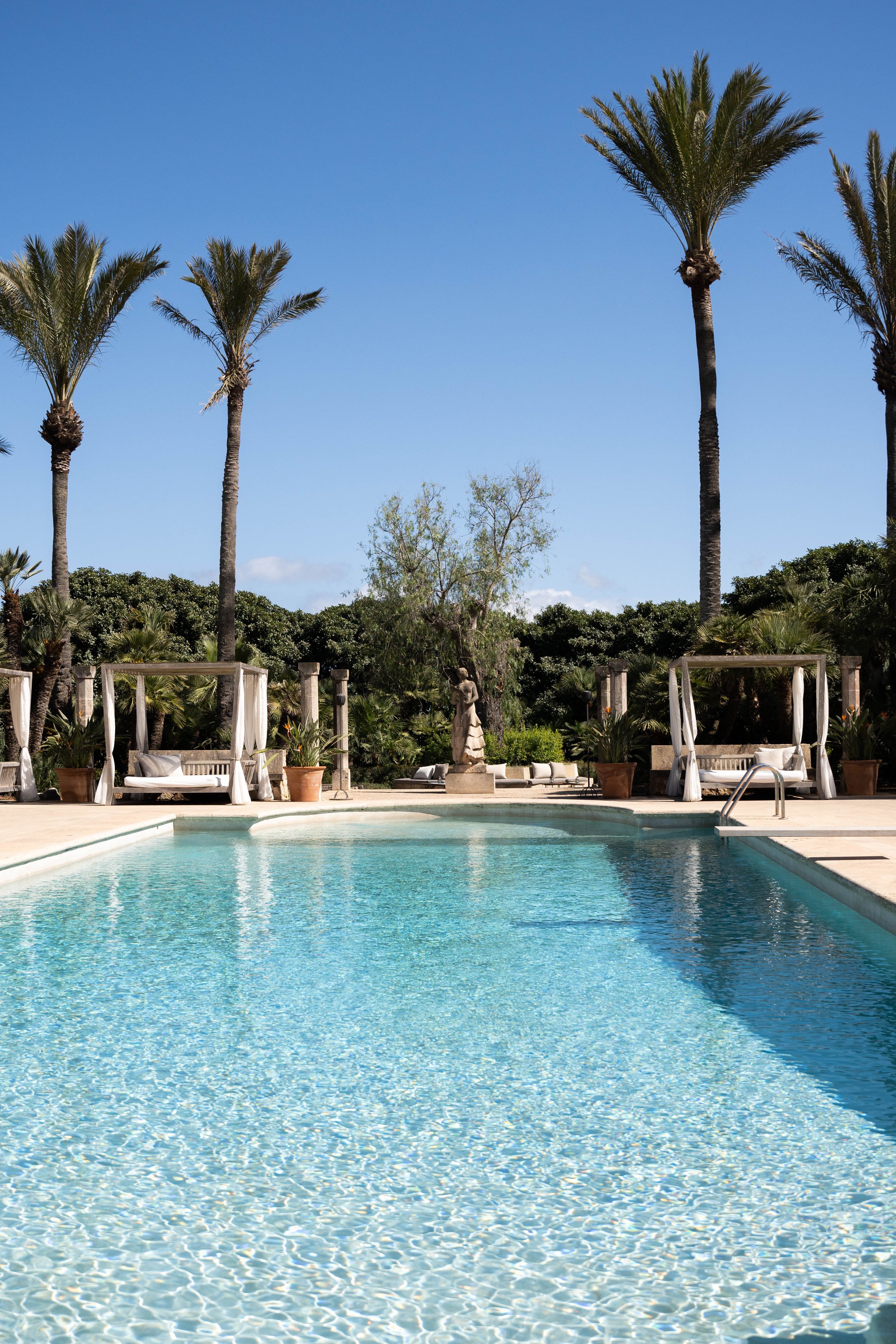 Poolområde med palmer og solsenge under en blå himmel
