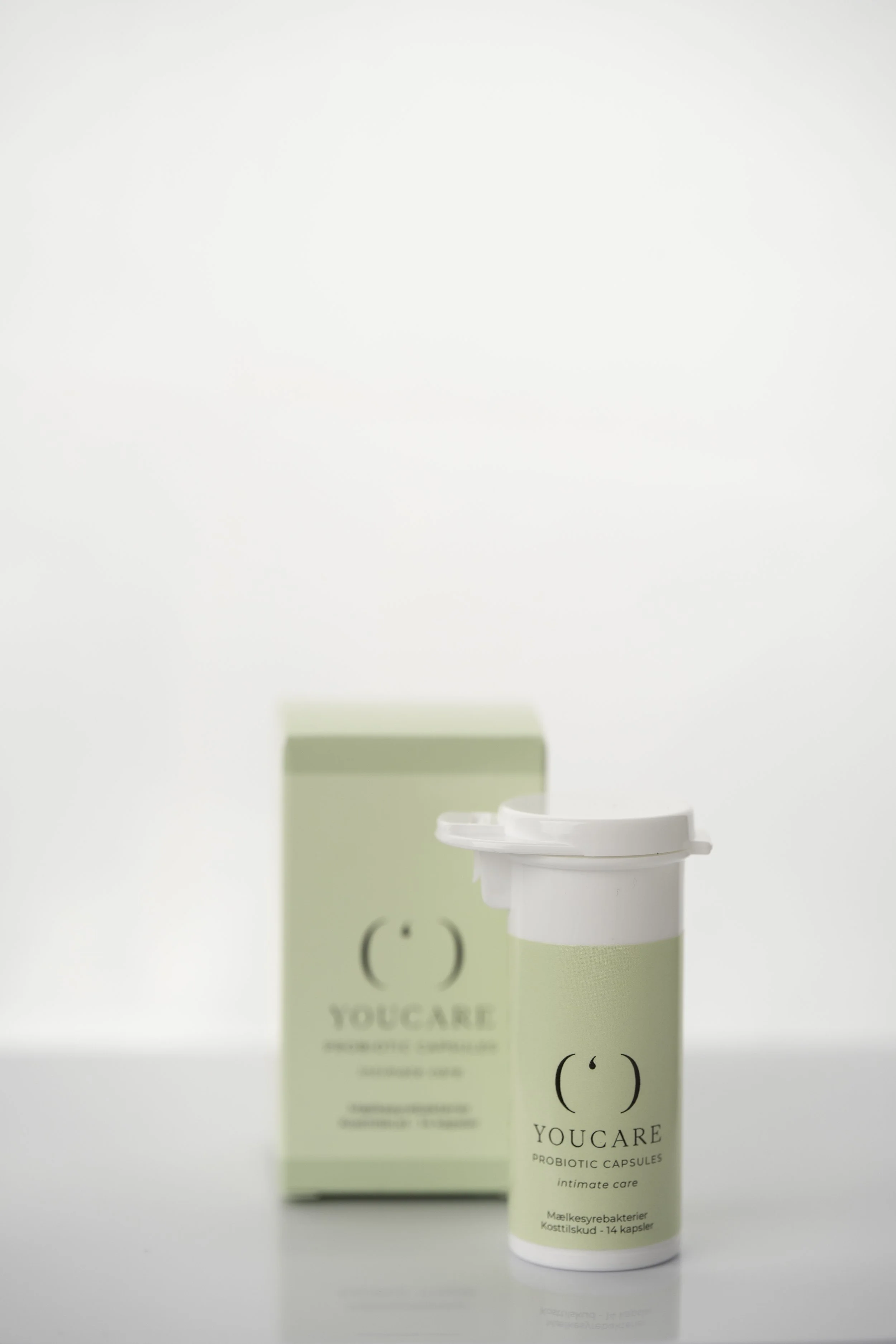 Kapsler fra YOUCARE, med grøn og hvid emballage, placeret foran en matchende boks.
