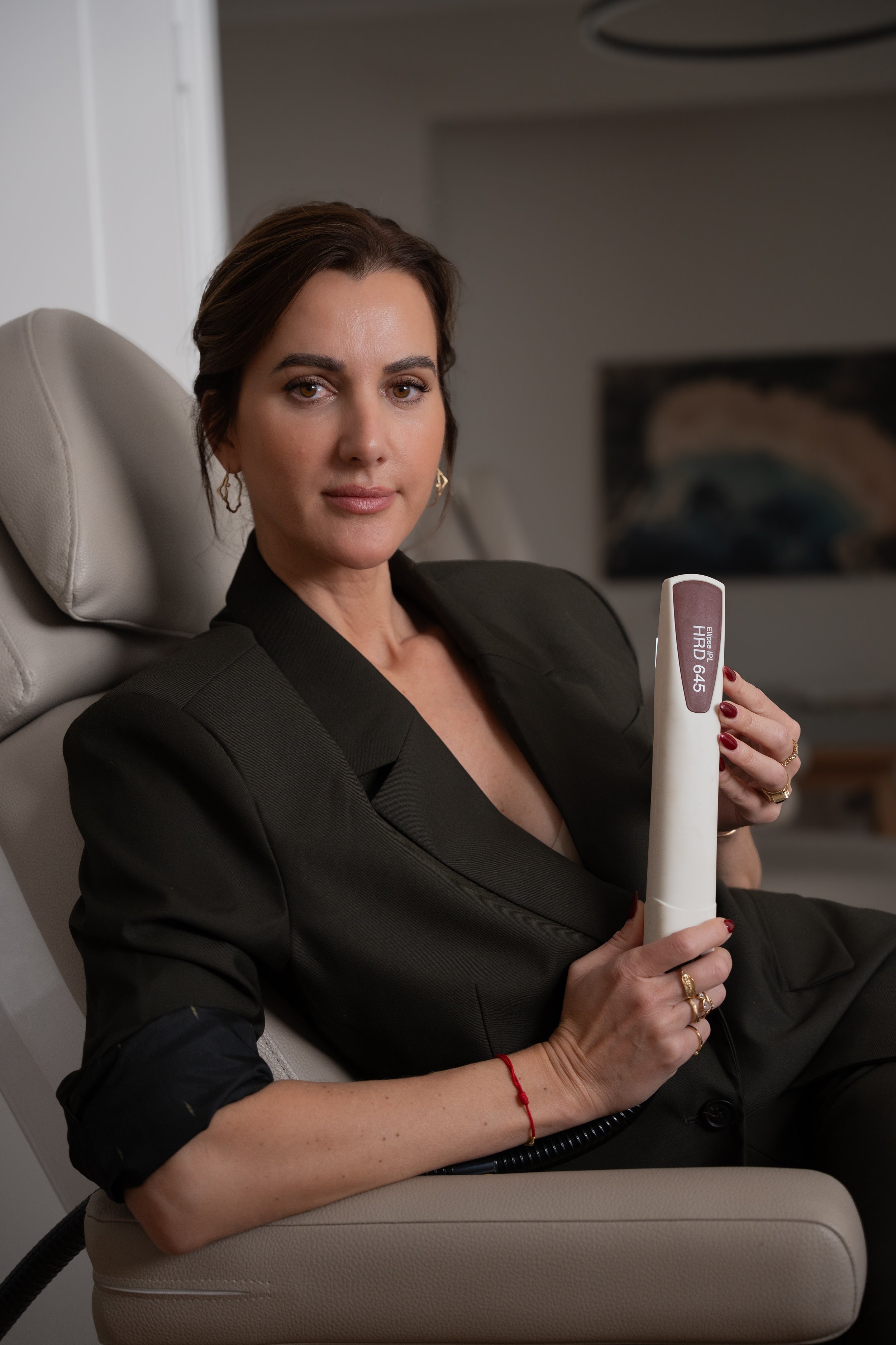 En kvinde sidder på en medicinsk stol, holder et laser hoved, og kigger seriøst mod kameraet.