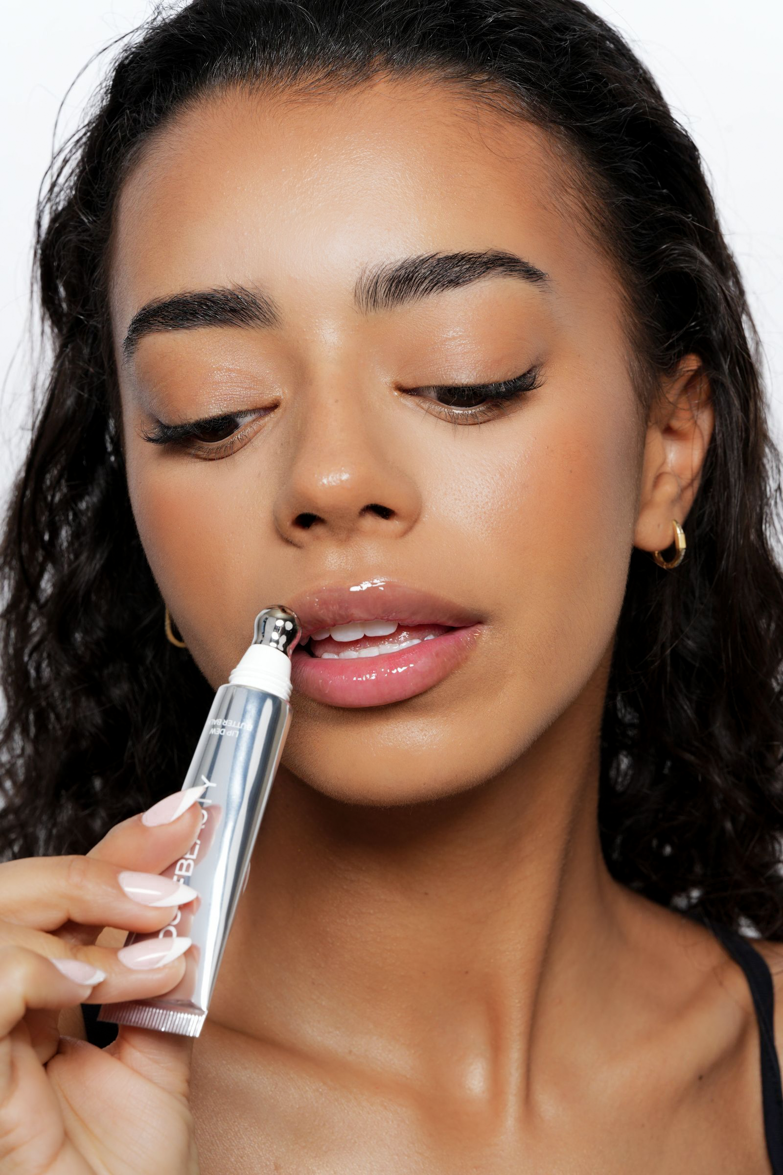 Kvindelig person med mørkt, bølget hår bruger en lipgloss på læberne.