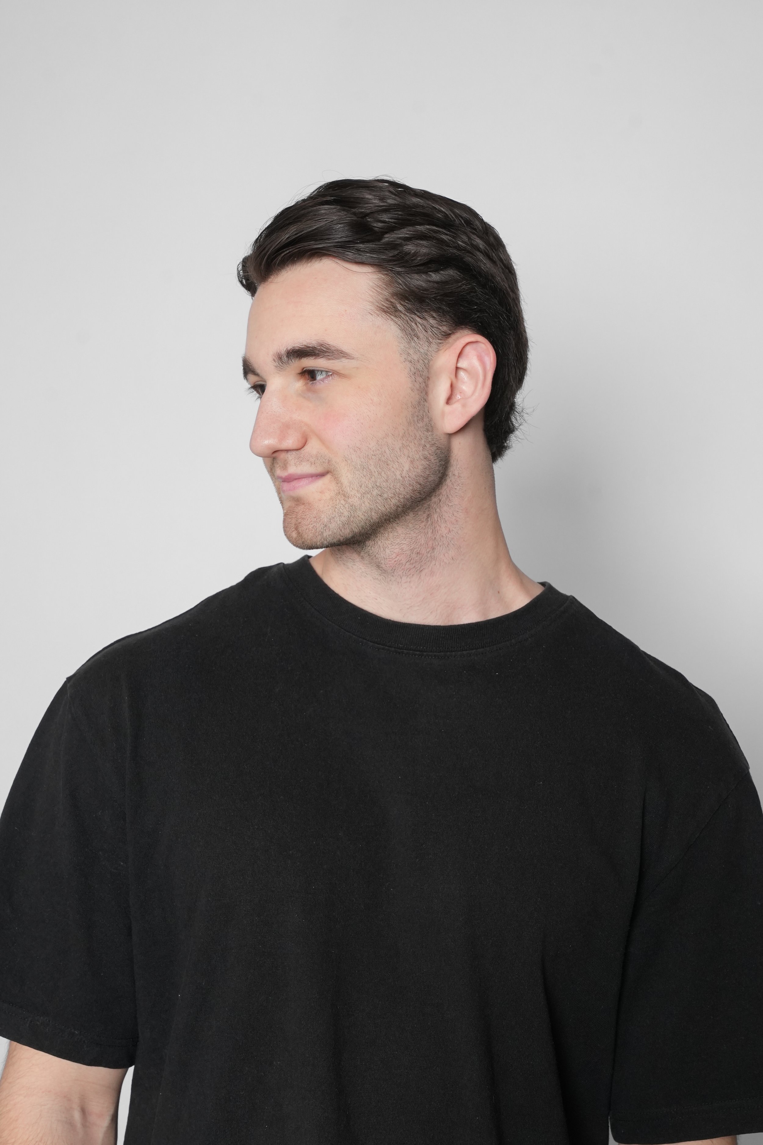 Ung mand med mørkt hår og sort T-shirt ser til venstre med hagen vendt væk fra kameraet.