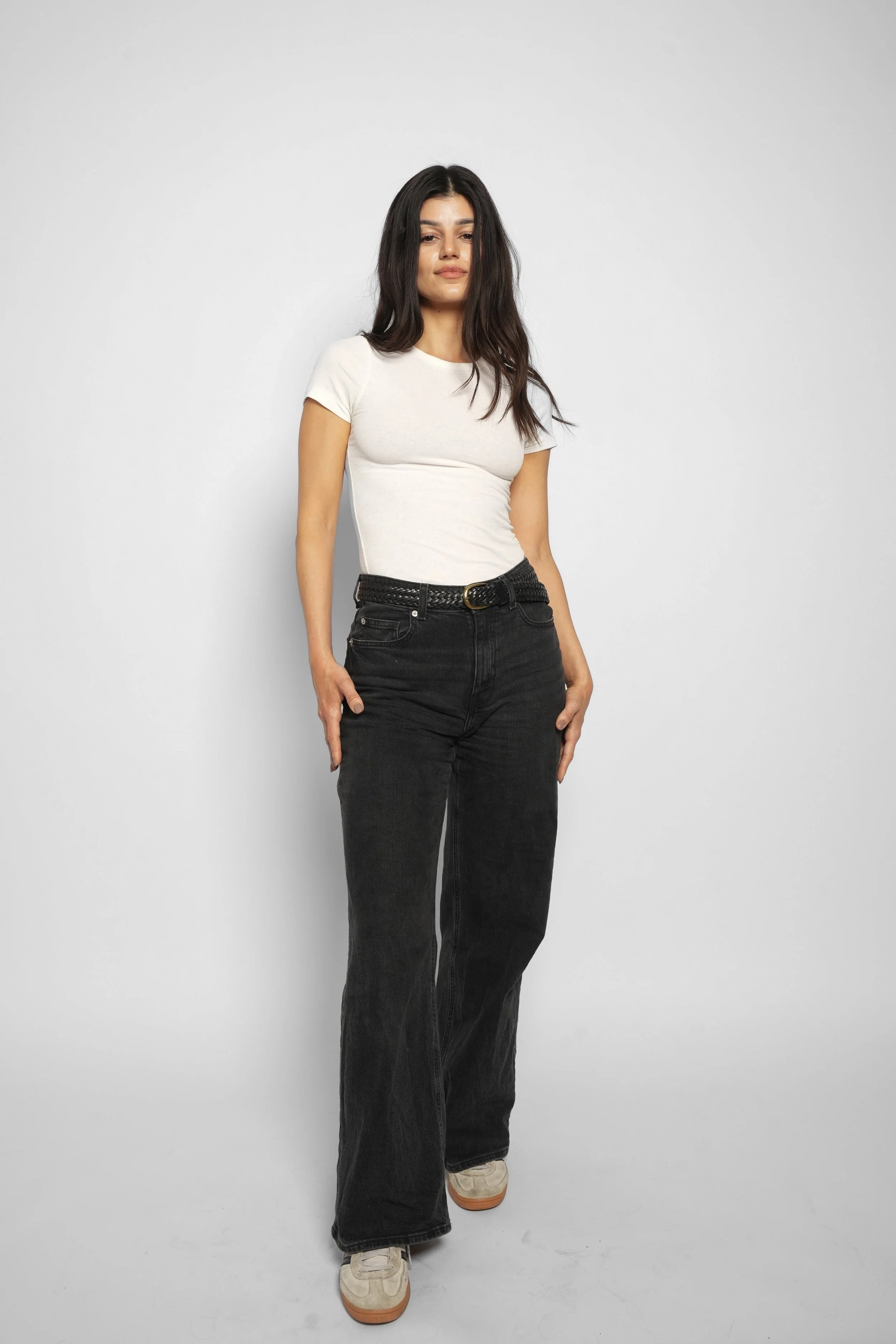 Kvinde i hvid T-shirt og sorte bukser står foran en hvid væg.