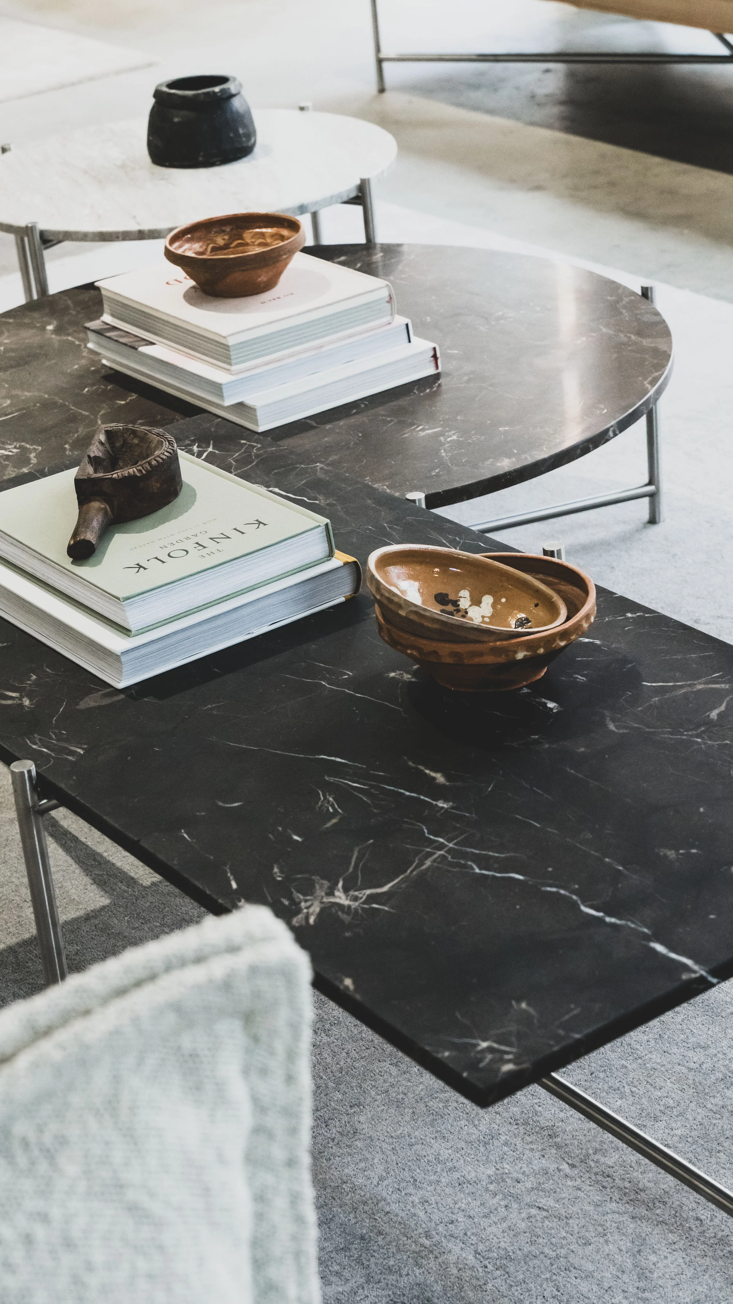 To sorte marbleborde med bøger og keramikskåle på, og en grå stol i forgrunden.