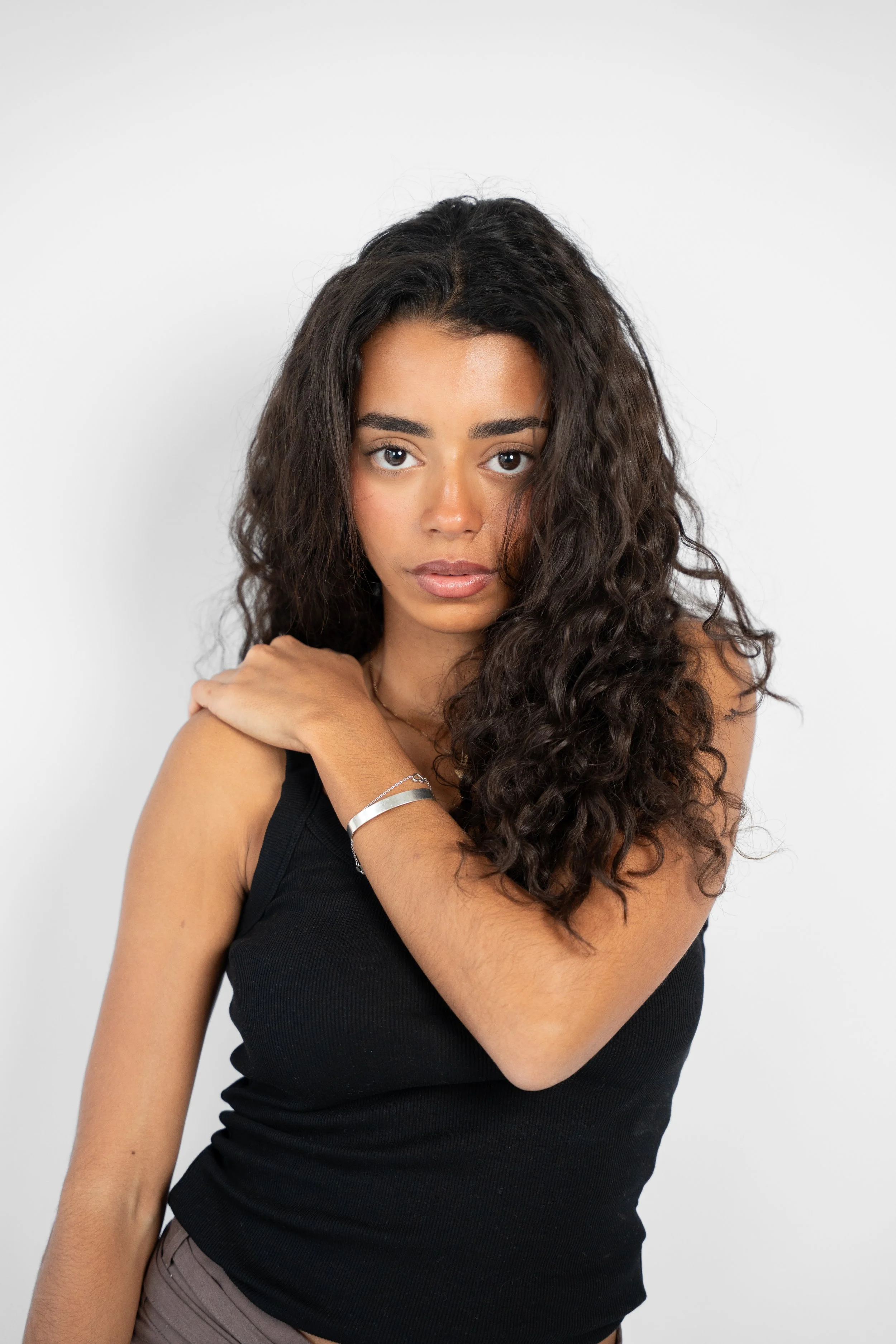 Et portræt af en ung kvinde med mørk, krøllet hår, iført sort top, inden for en neutral baggrund.