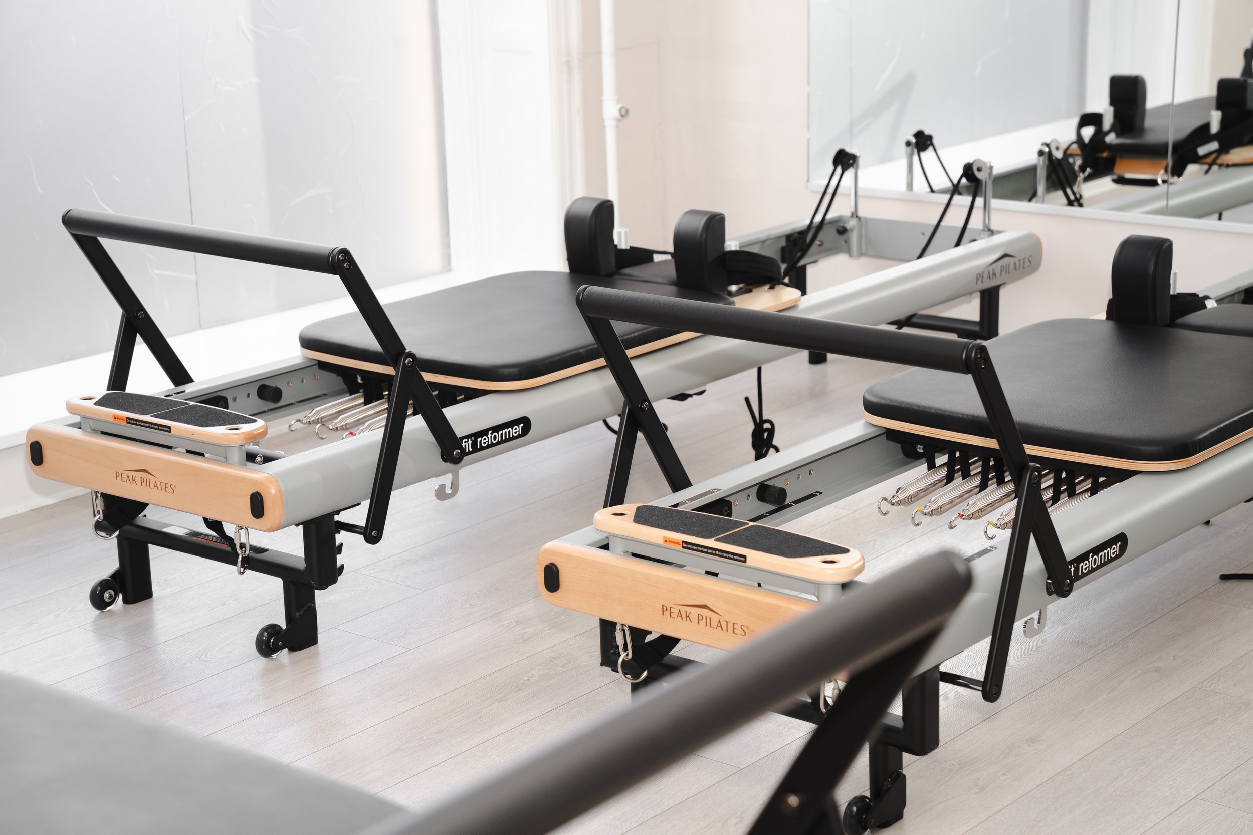 To reformermaskiner med sort polstring og trærammer i et træningslokale.