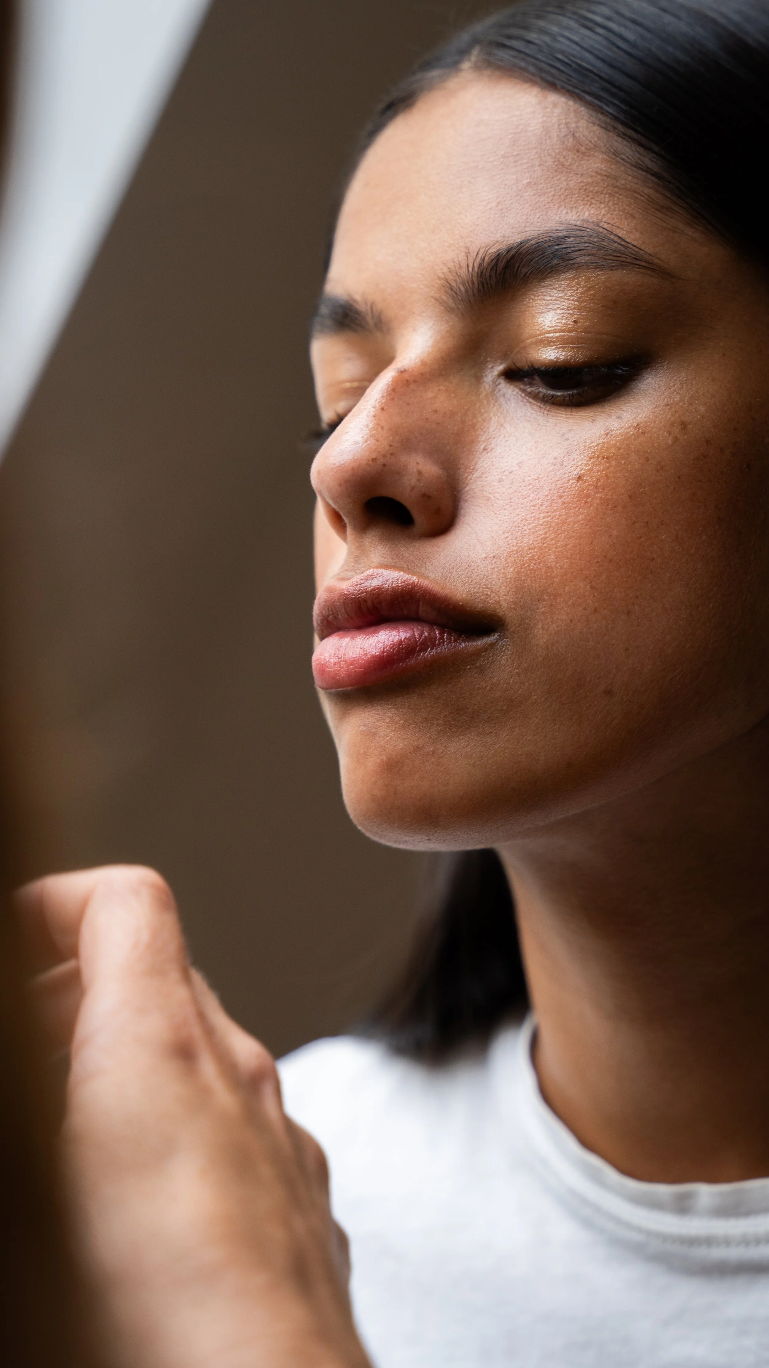 Nærbillede af en ung kvinde, der anvender make-up, med fokus på hendes ansigt og hånd, der holder en makeup børste.