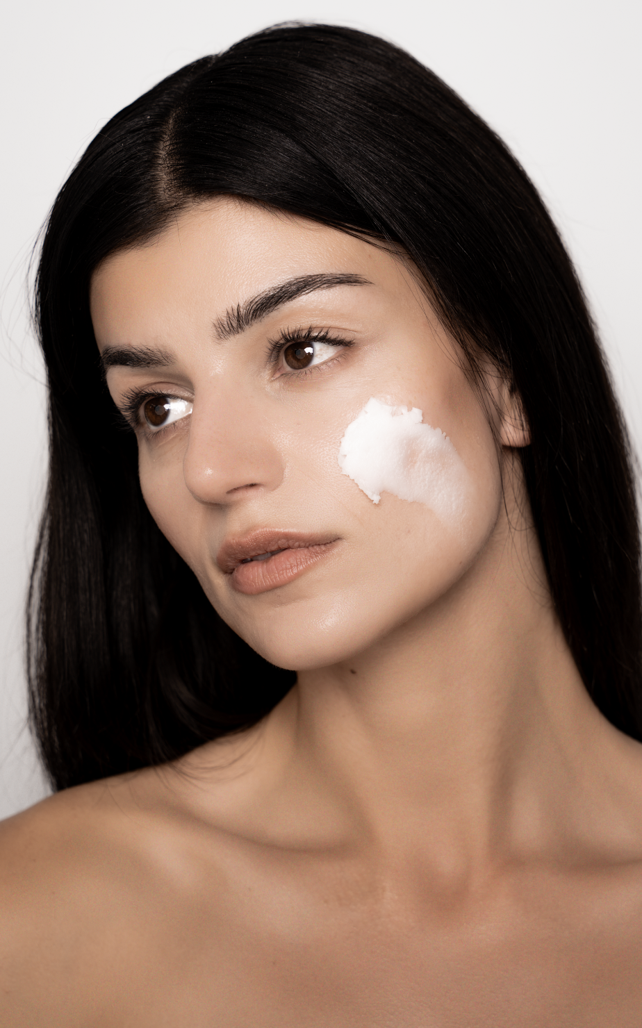 Kvinde med mørkt, langt hår, der har creme på kinden.
