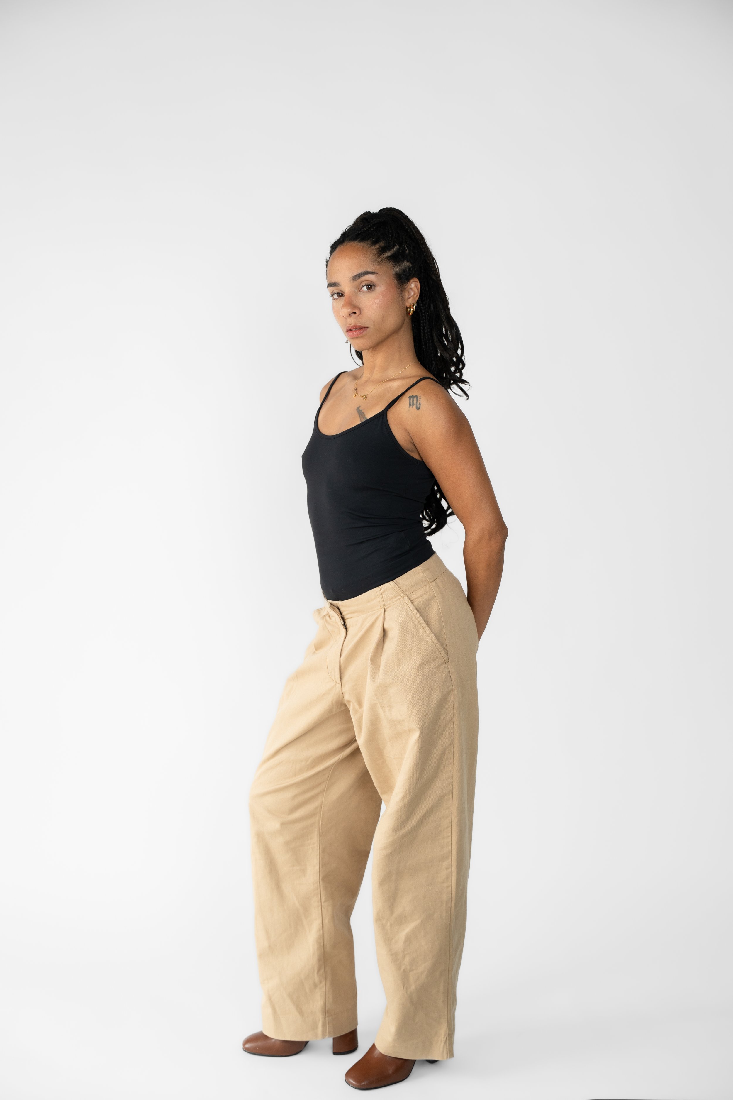 Kvinde står i beige bukser og sort top mod en hvid baggrund.