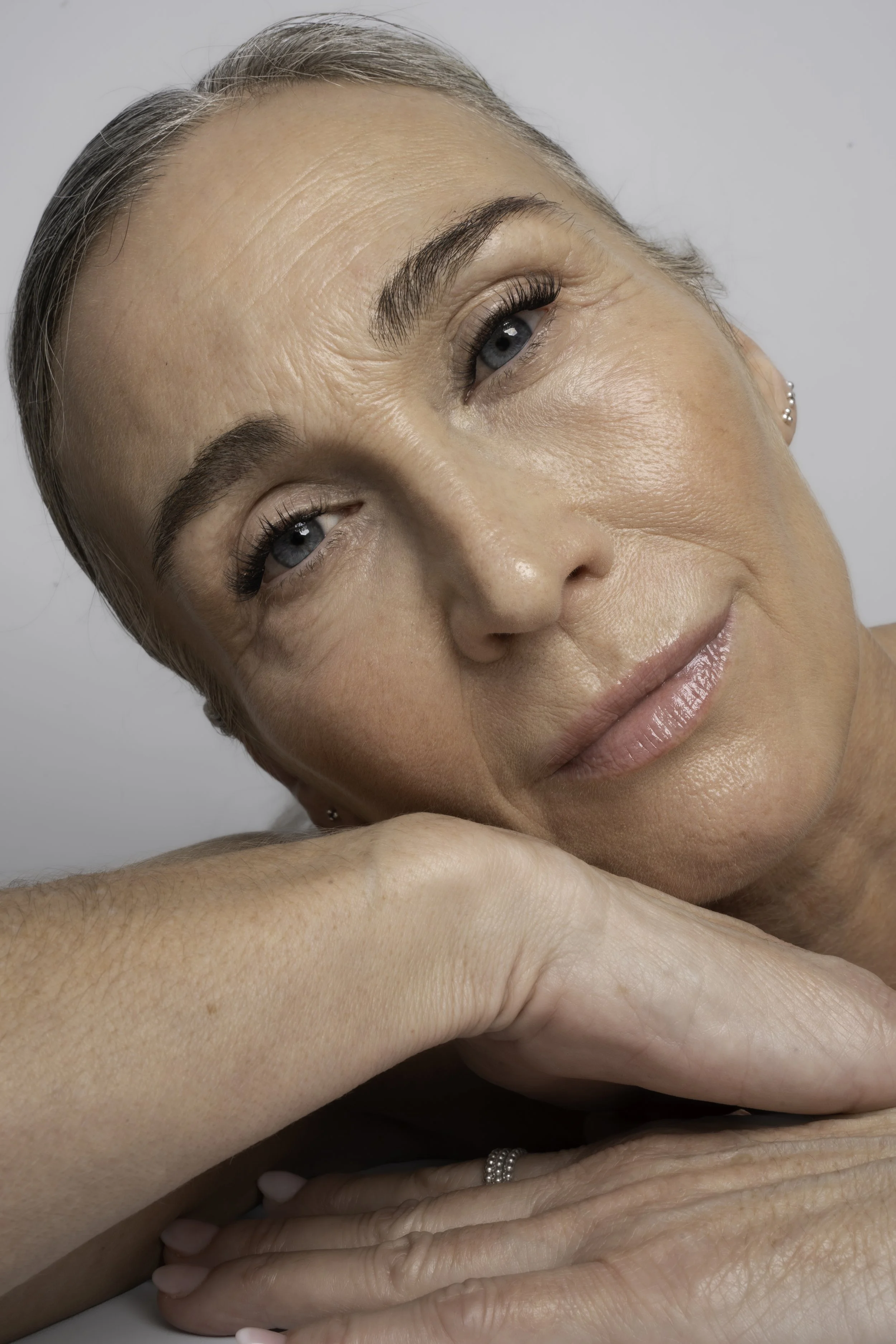Nærbillede af en rolig ældre kvinde, der hviler sit hoved på sine arme, med fokus på hendes ansigt og hænder.