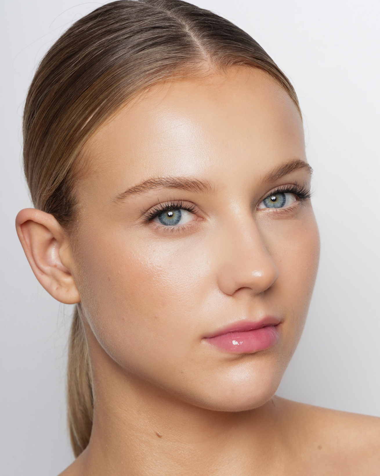 Nærbillede af en ung kvindes ansigt med glat hud og lyse øjne.