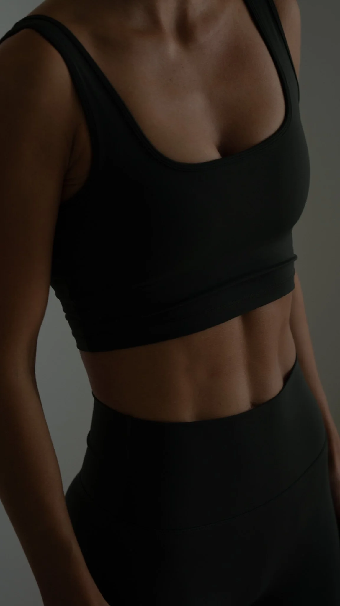 En kvinde iført sort sports-bh og leggings, der viser sin mave og veldefinerede mavemuskler.