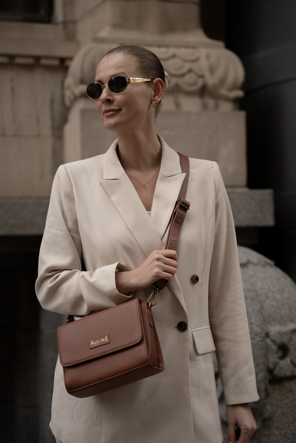 Kvinde iført beige blazer, solbriller, og med brunt kosmetiktaske fra Alvité.