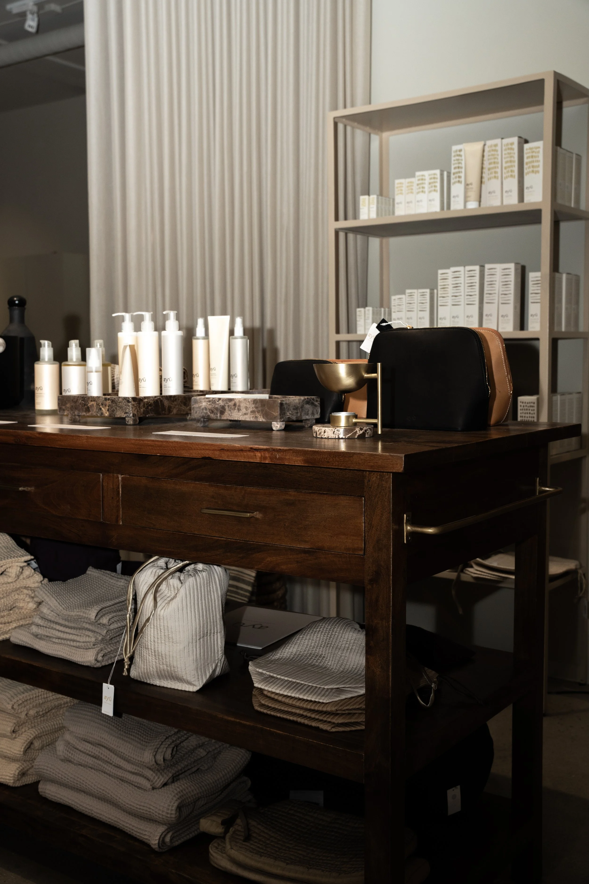 Interiør af en butik med hylder og produkter, herunder hånd- og kropsplejeprodukter, tasker, og tekstiler.