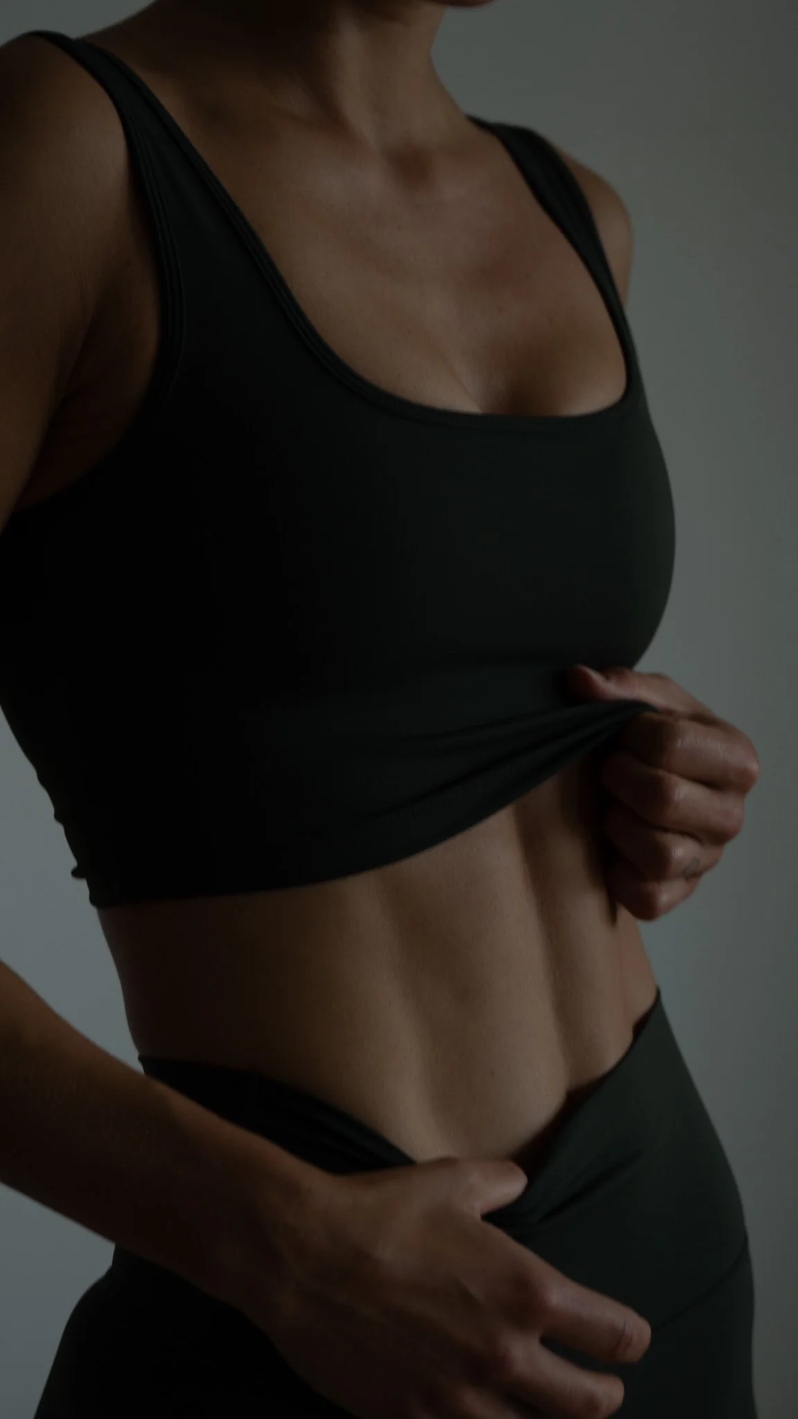 Nærbillede af en person, der løftes toppen for at vise maven, iført sort træningstøj.