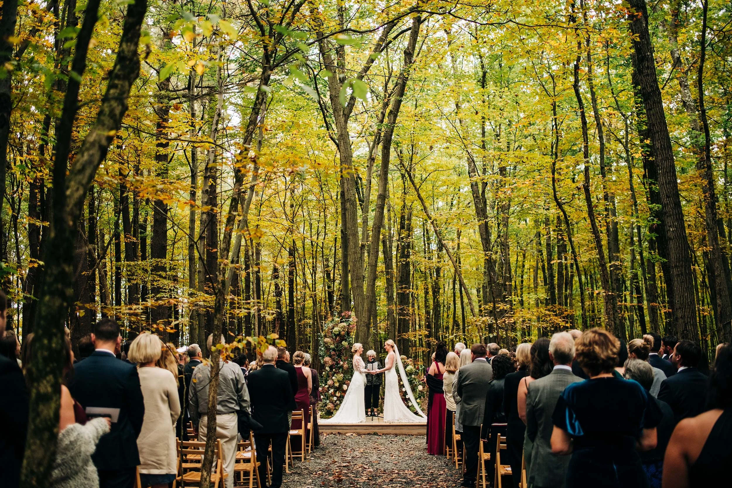 Two brides exchanging vows in a forest during peak fall foliage_Alexandra Roberts