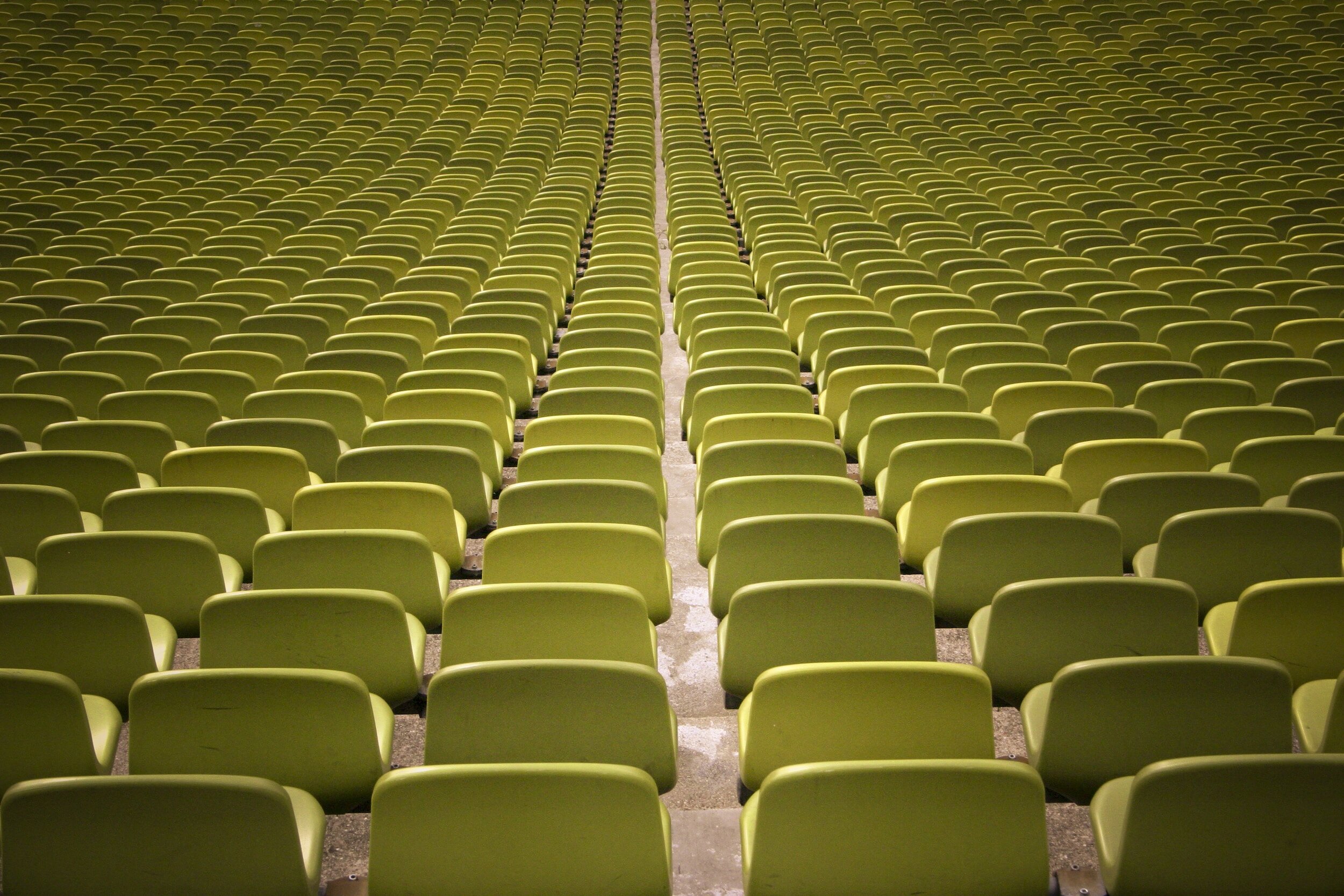 A large empty auditorium or stadium with many rows of lime green seats arranged in a curved pattern and a central aisle.