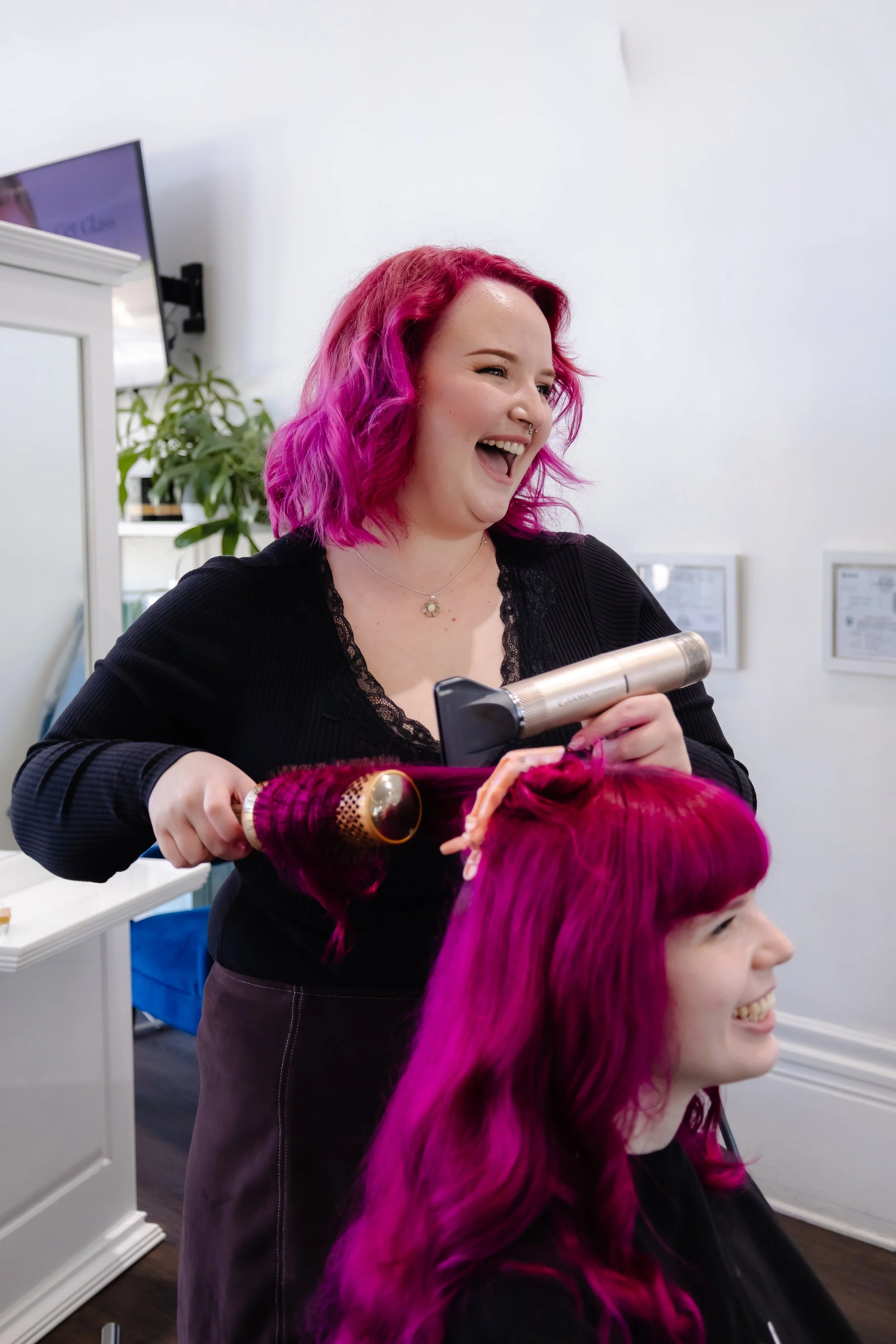 Hot pink haired stylist curling her client's hair.