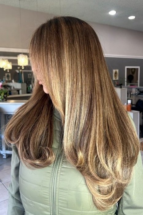 woman shows a side profile of her long, freshly blowwaved caramel blonde highlighted hair