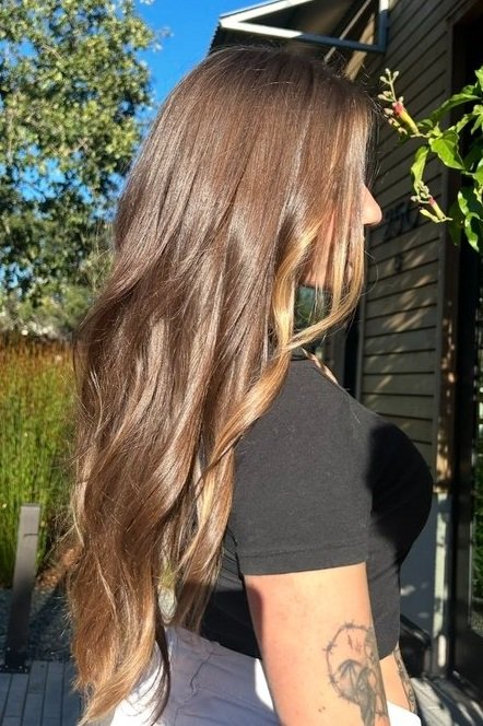 side profile of woman in black tshirt with slightly curled long caramel brown hair