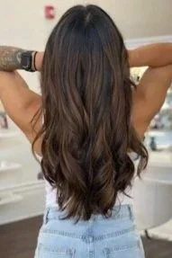 woman standing in salon holds up hair showing freshly dyed brown long curled hair