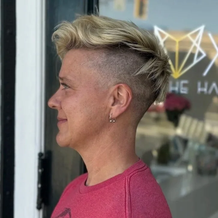 woman wearing pink shirt stands sideways showing short blonde haircut and fade