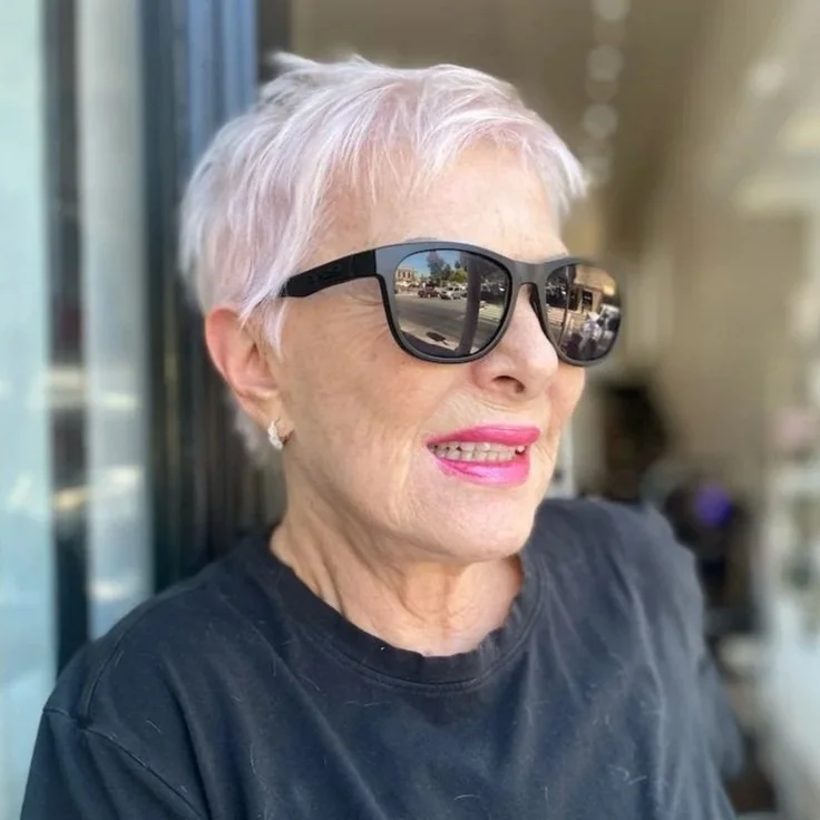 older woman with pink short pixie haircut wears sunglasses ooutside hairsalon
