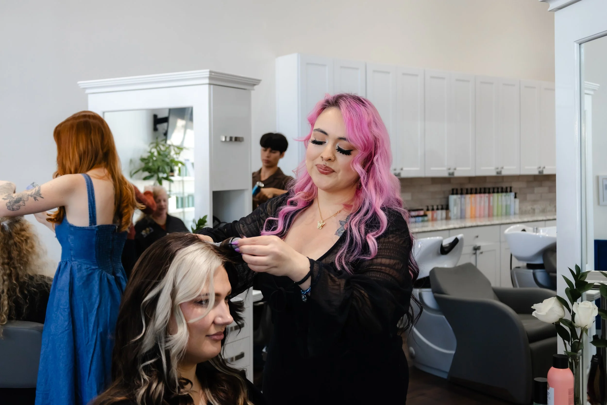 Girl with pink hair curling her client's hair.