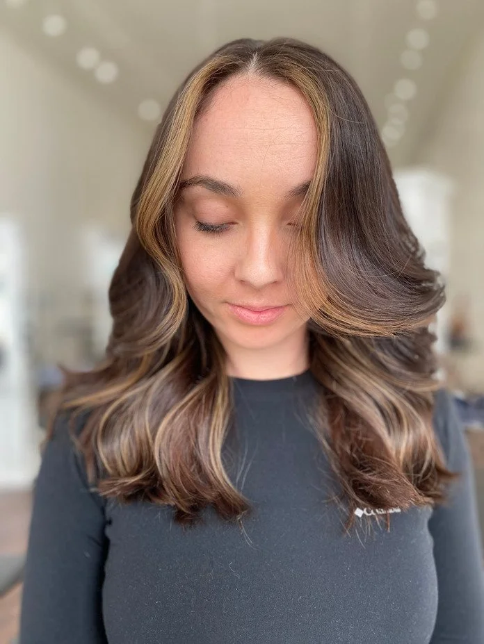 young girl faces camera with brown hair and front caramel highlights in hair salon