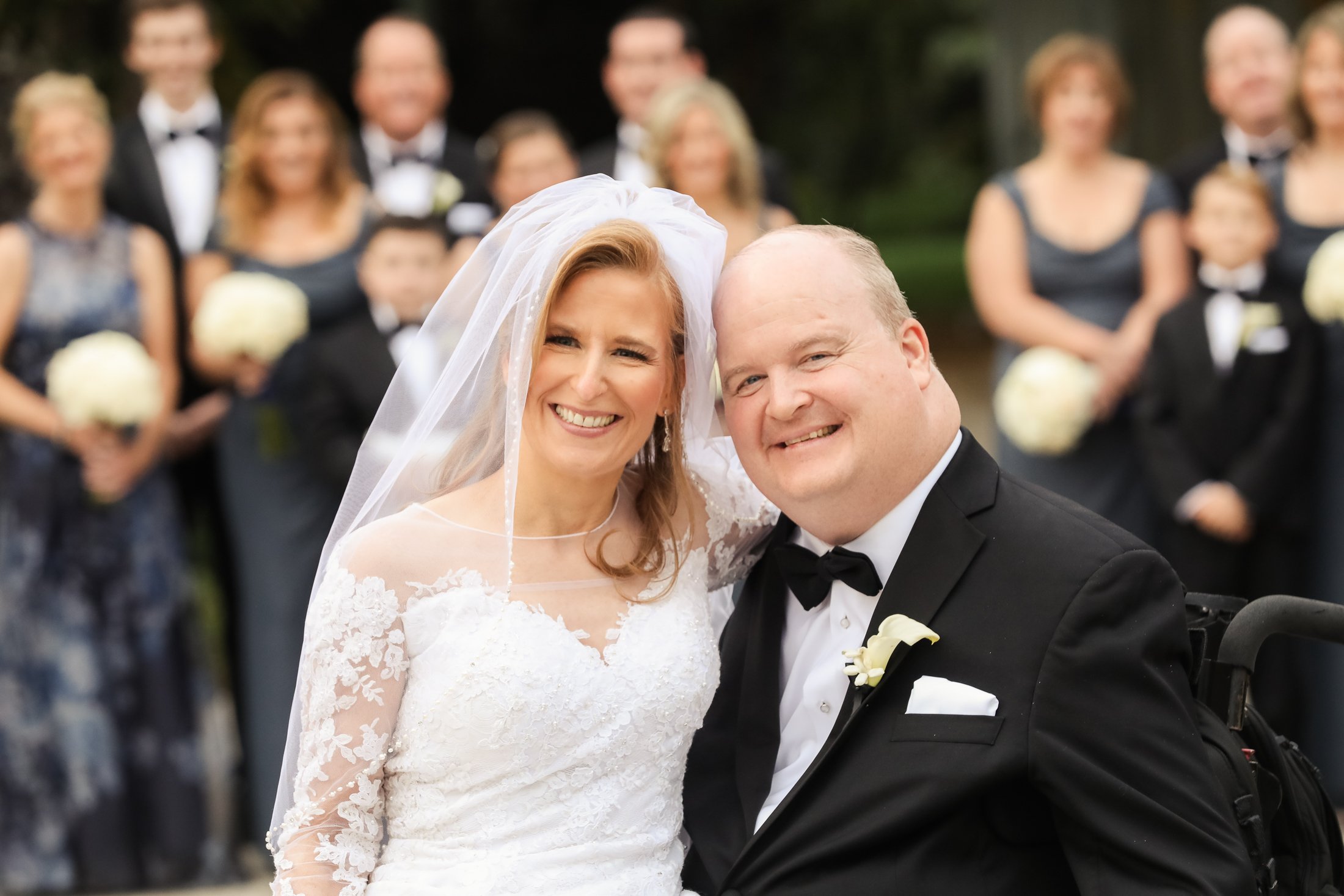 Bride and groom smiling at each other during their wedding celebration, with guests in formal attire in the background.