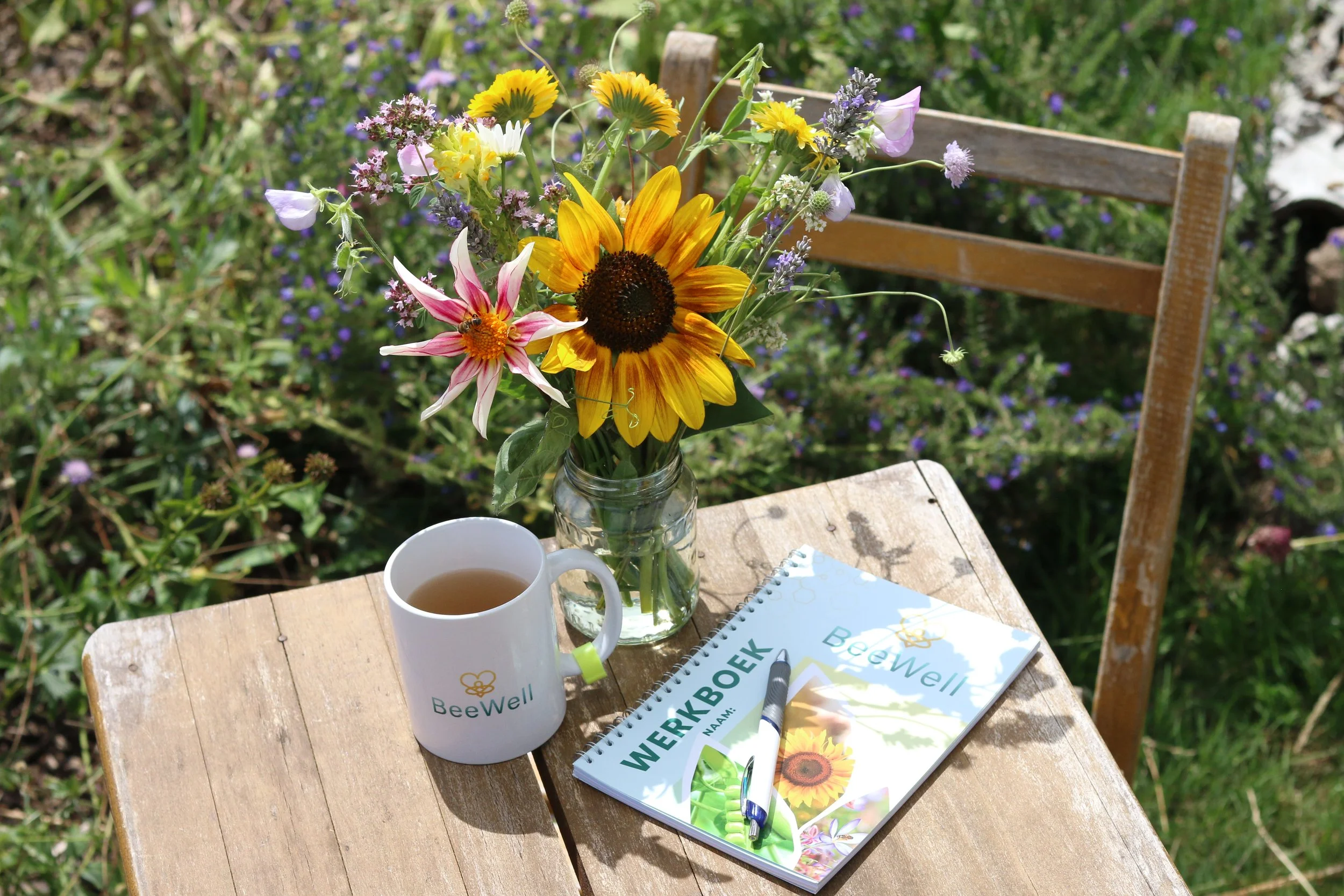 Een zonnebloem en bloeiende planten als decor voor het werkboek re-integratie in de Beewell-tuin
