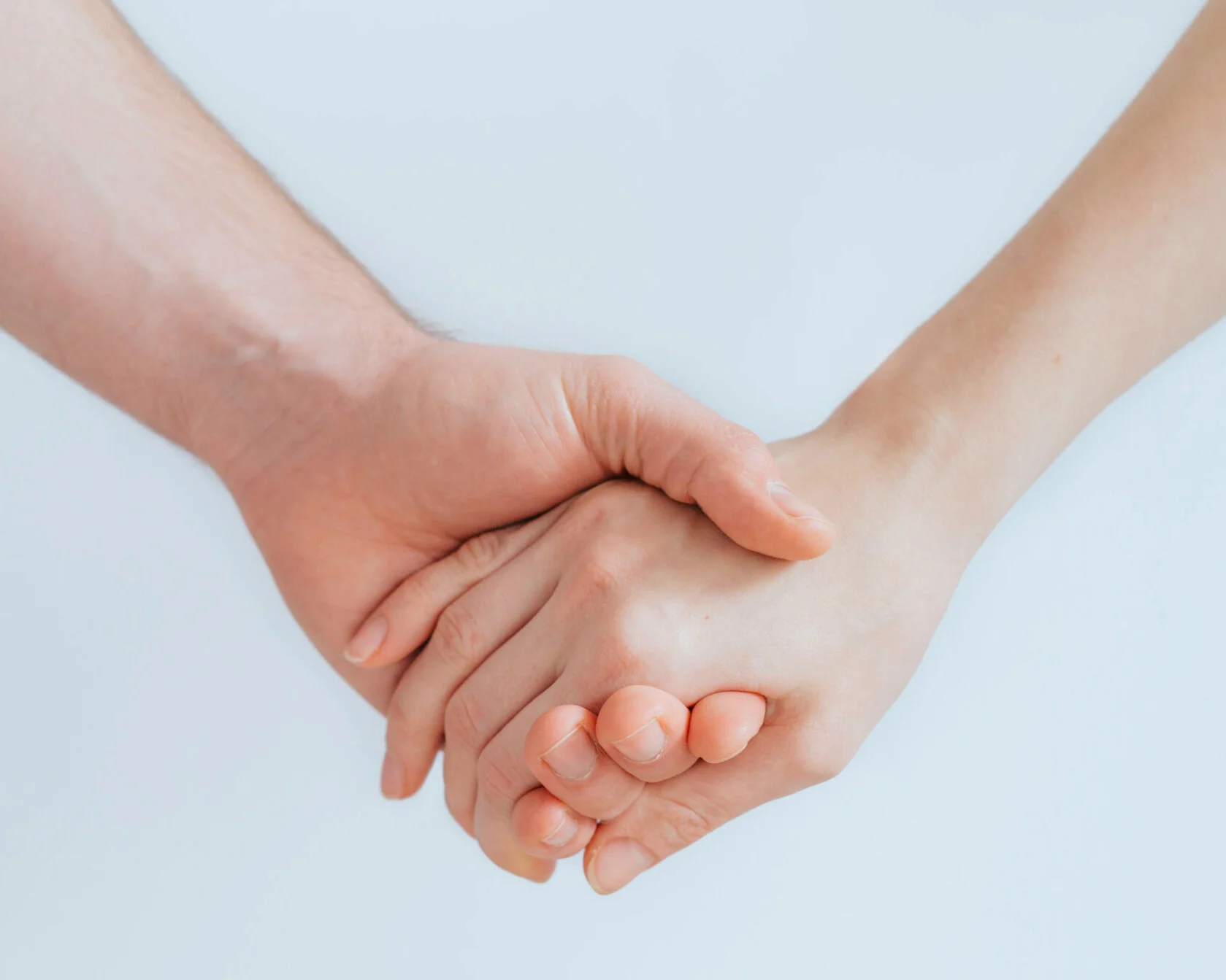 Two people holding hands against a plain light background.