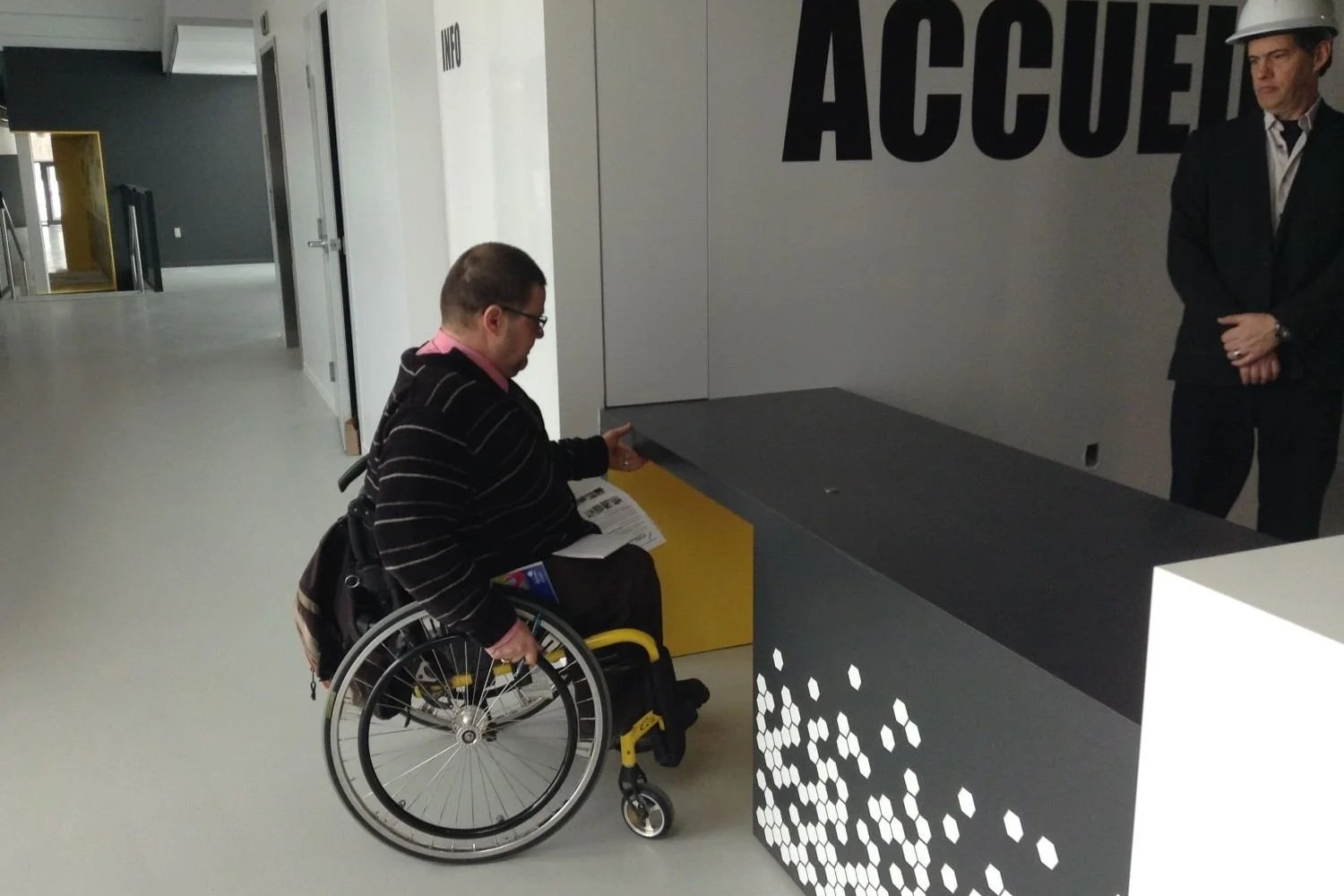 Utilisateur de fauteuil roulant à l'accueil (comptoir évidé pour s'approcher) du centre communautaire Lebourgneuf. 