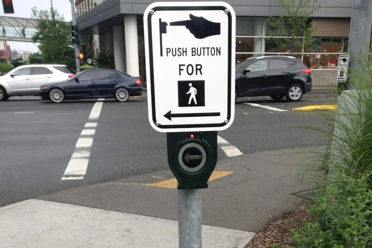 Bouton d'appel à une intersection. Un panneau indique la direction de la traverse, tout comme la flèche surélevée sur le bouton.