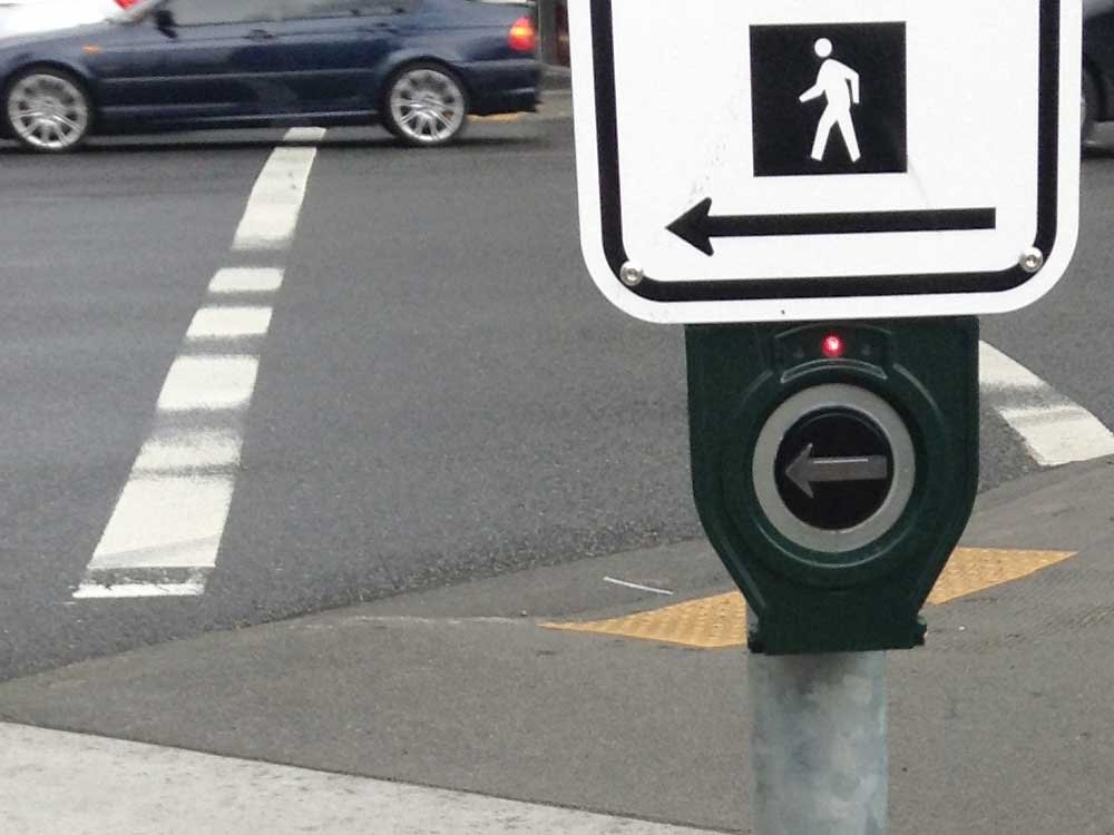 Bouton d'appel à une intersection. Un panneau indique la direction de la traverse, tout comme la flèche surélevée sur le bouton.