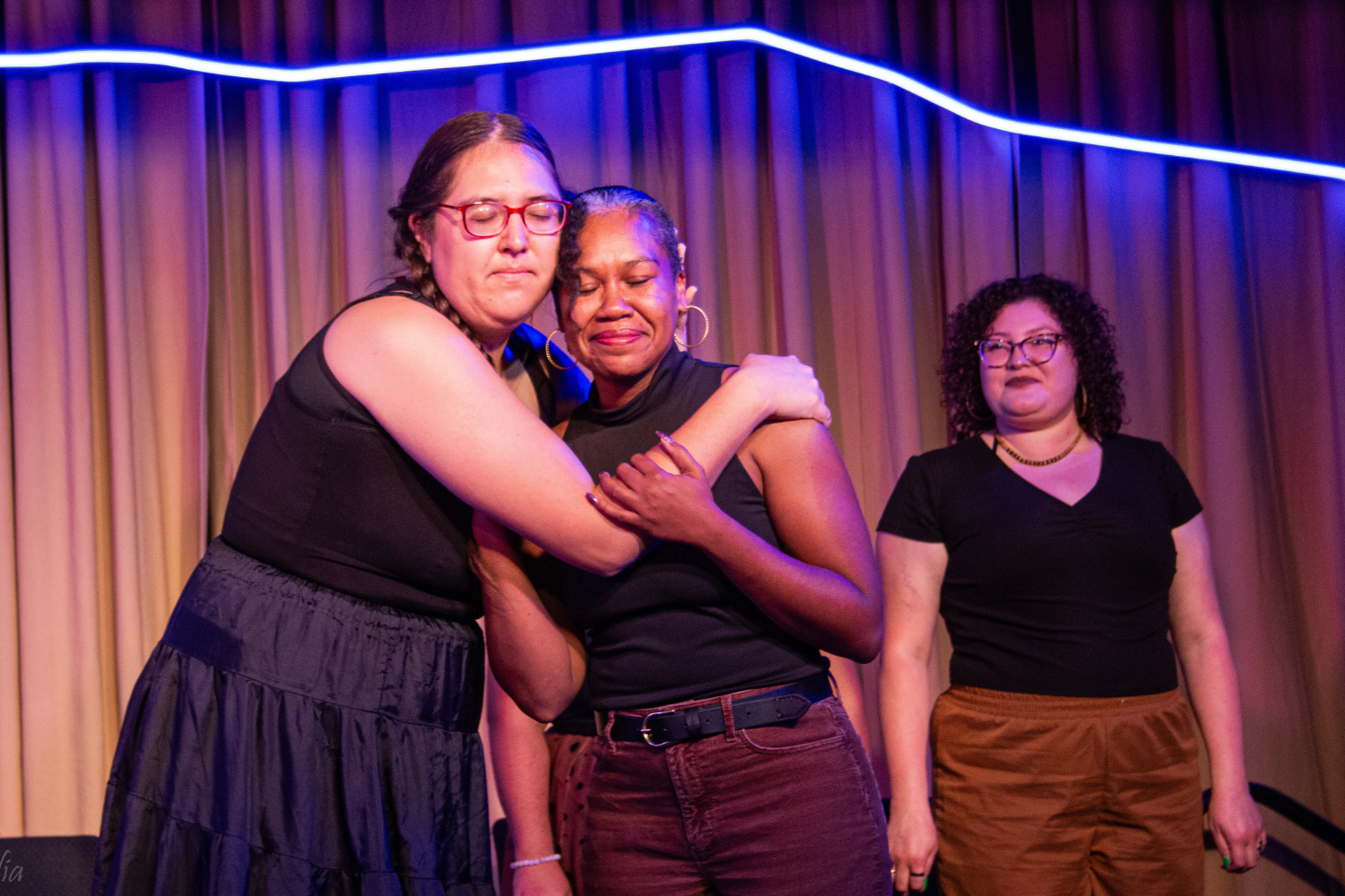3 Playback Theatre performers of different races on stage, all are smiling, 2 are embracing