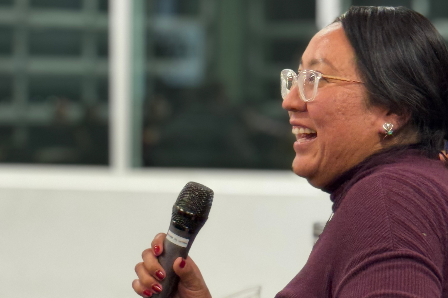 A woman smiles while holding a microphone and telling her story