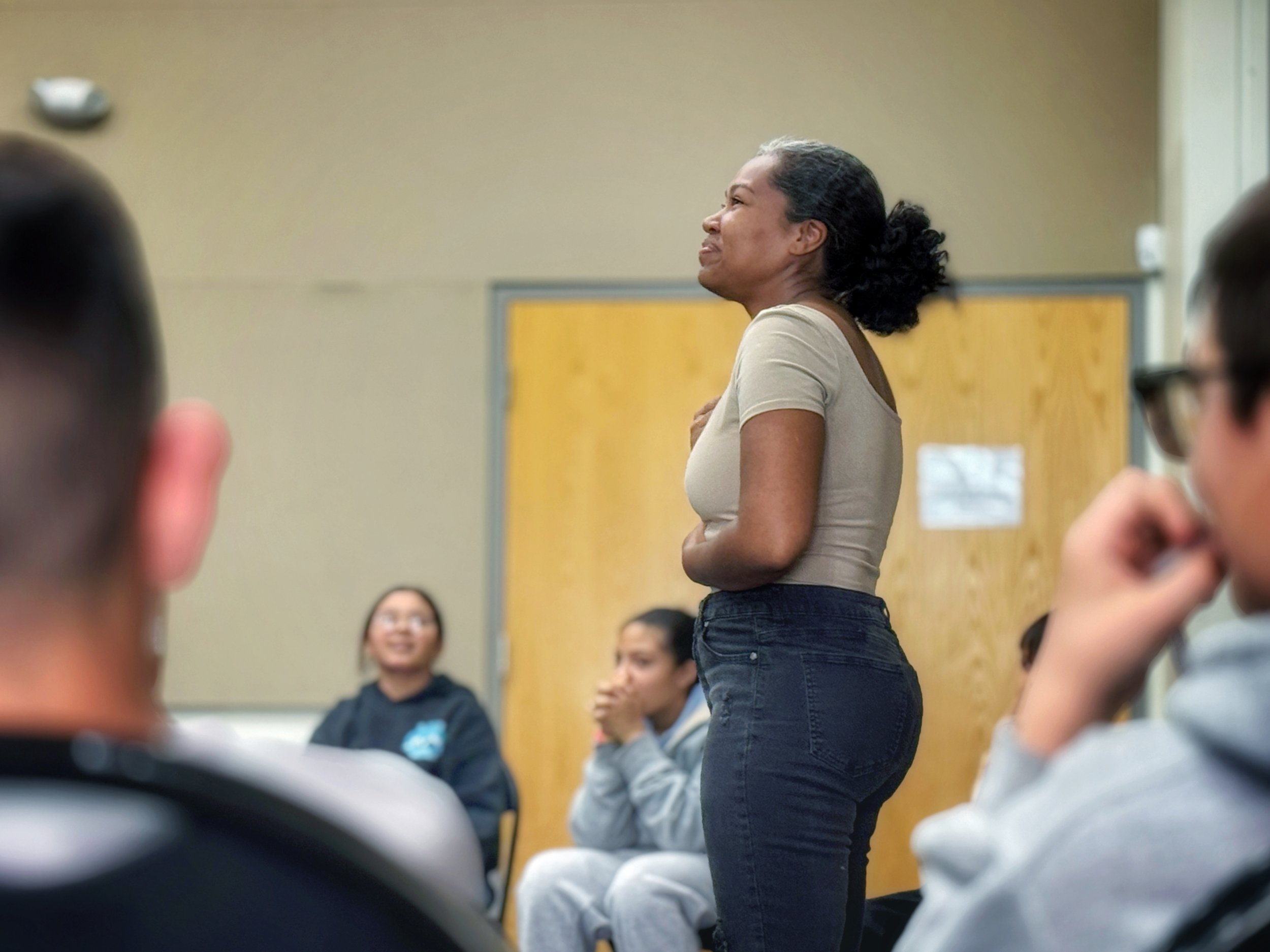 An actor is in a circle of young people, smiling and putting her hands to her chest, wistful