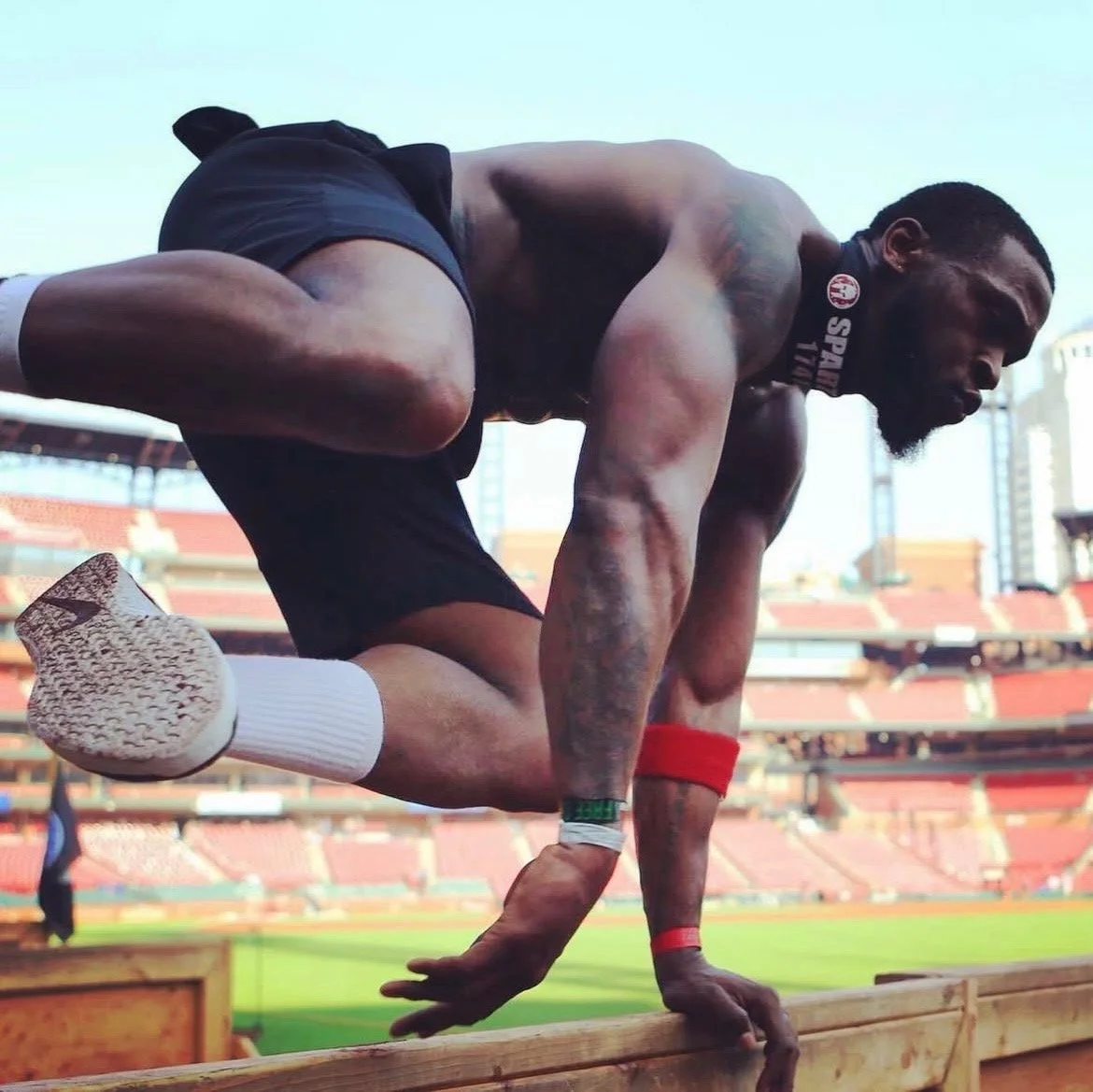 Man doing a box step-up with a dumbbell in a gym, wearing a red T-shirt.