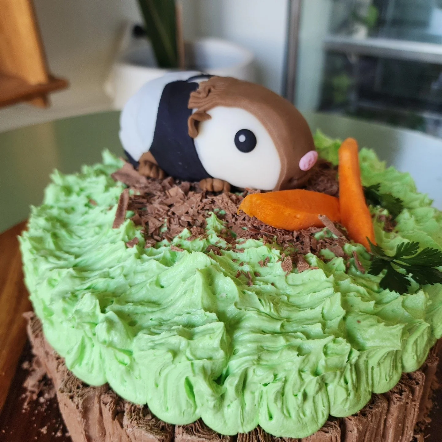 A cake decorated to look like a character from the movie Finding Nemo, with green frosting, chocolate shavings, and orange carrot slices, topped with a fondant figure of Nemo.
