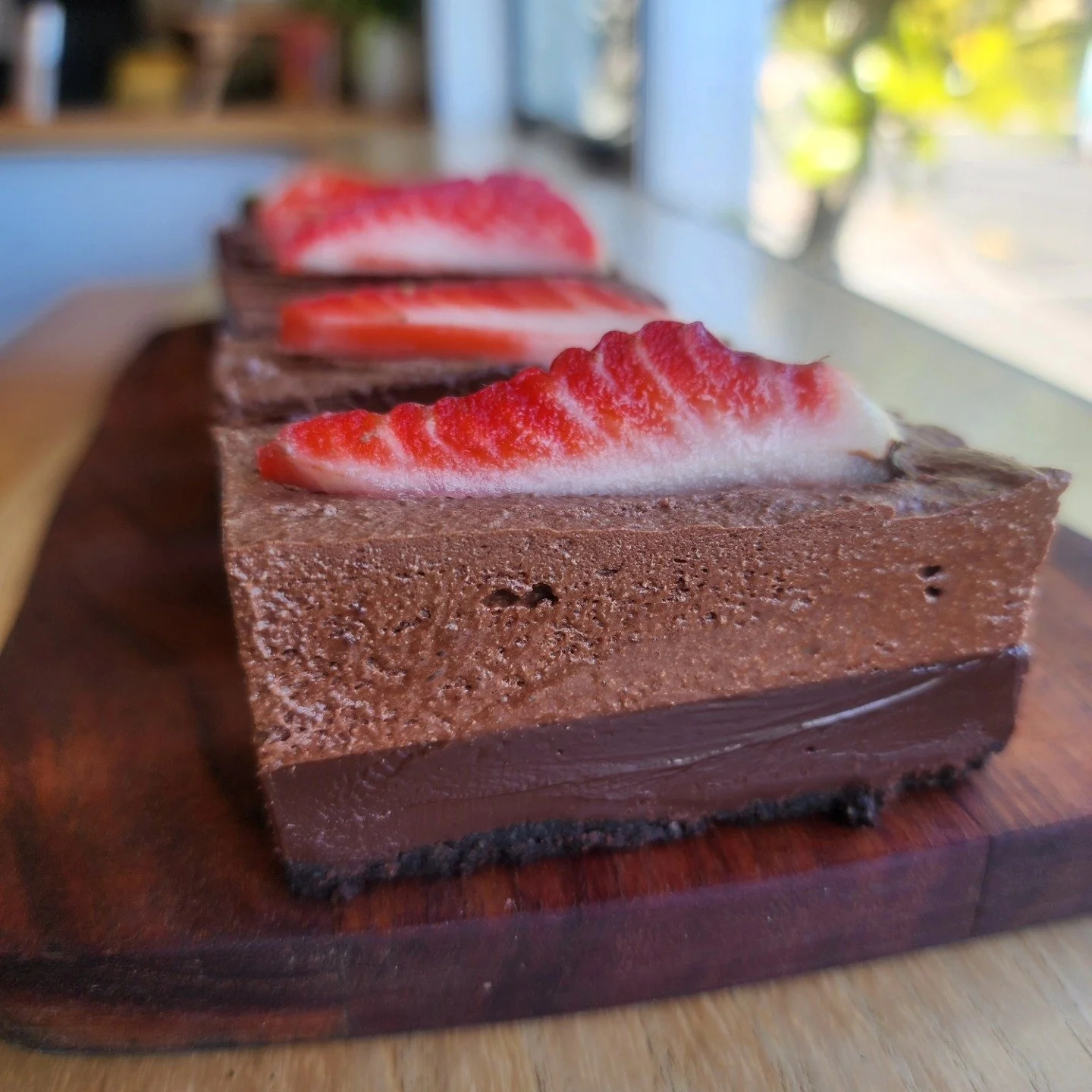 Close-up of a layered chocolate cake with strawberry slices on top, on a wooden serving board.